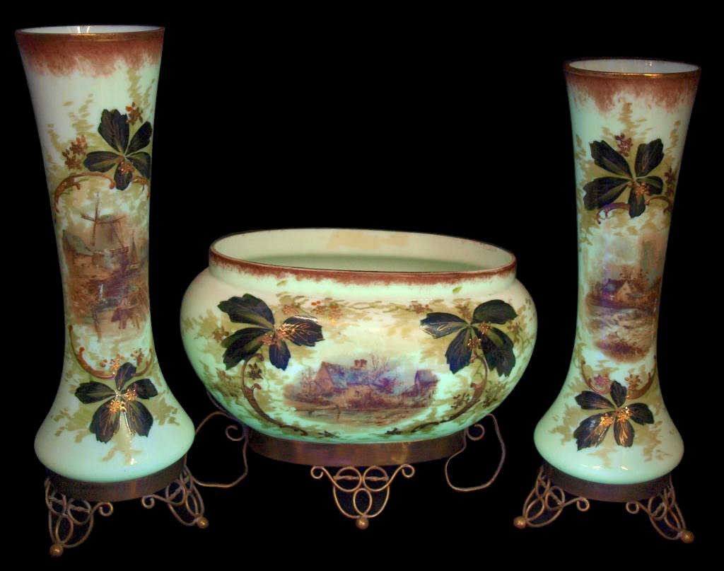 FINE ANTIQUE PARCEL GILT BRISTOL GLASS MANTLE SET: (set of 3) Fine Bristol glass mantle set fluorescing under a blacklight, comprising (1) oval center bowl and (2) garniture vases, custard color ground with transfer decorated scene enclosed by hand pa