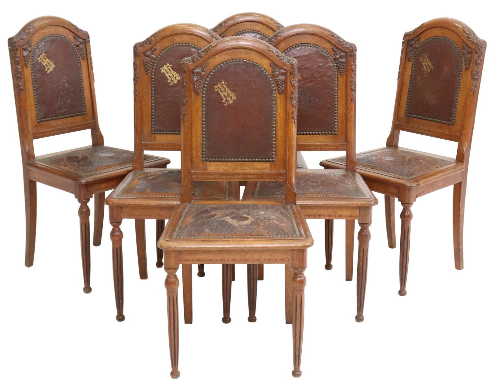 6) ART NOUVEAU CARVED OAK & LEATHER DINING CHAIRS: (lot of 6) French Art Nouveau carved oak dining chairs, early 20th c., having arched back carved with fruit and foliate motifs, in worn embossed leather upholstery, rising on fluted tapered supports, 