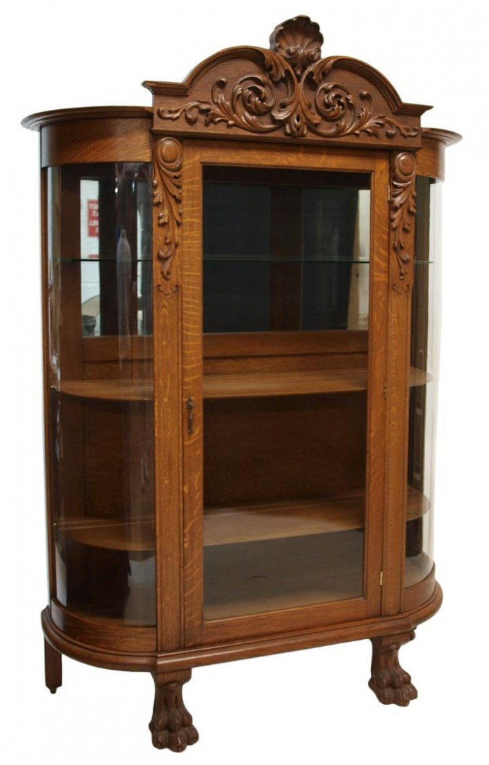 AMERICAN OAK CURVED GLASS CHINA CABINET: American quarter sawn oak display cabinet, c. 1900, a central cornice with applied carving over the flat glass door flanked by curved glass, the interior with partial mirror back, two adjustable wood 