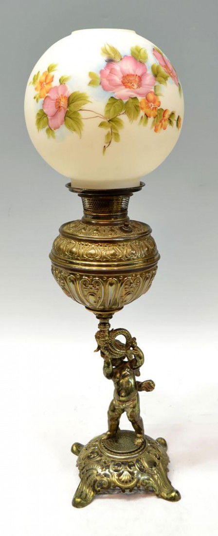 BRASS BANQUENT LAMP, EDWARD MILLER, ELECTRIFIED: American brass banquet oil lamp, c. 1900, marked E.M. & Co. (Edward Miller & Company, Meriden Co.), floral painted globe over the foliate decorated brass pot supported by a winged putti holding a dolp