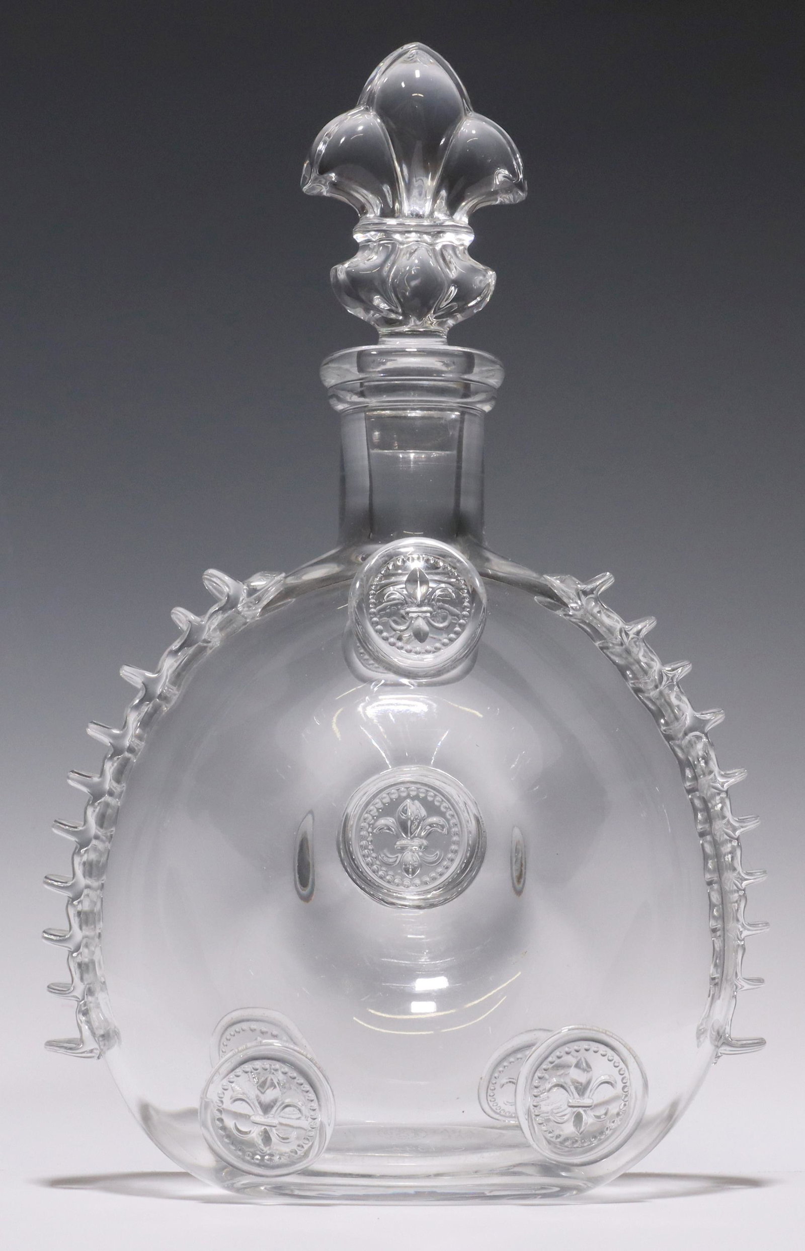 BACCARAT CRYSTAL REMY MARTIN LOUIS XIII DECANTER: Baccarat crystal Louis XIII cognac decanter, for E. Remy Martin and Company, having fleur-de-lis stopper, round bottle, with embossed fleur-de-lis motifs and ruffled sides, acid-etched mark underfoot,