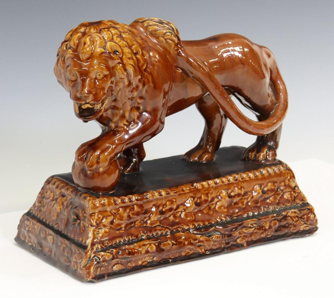 ENGLISH TREACLE-GLAZED POTTERY LION GARNITURE: English treacle-glazed pottery garniture, 19th c., modeled as a Medici lion with his front paw raised on a ball, stepped plinth base, chips along bottom edge and to one tooth, approx 11"h, 12.75"w, 6.