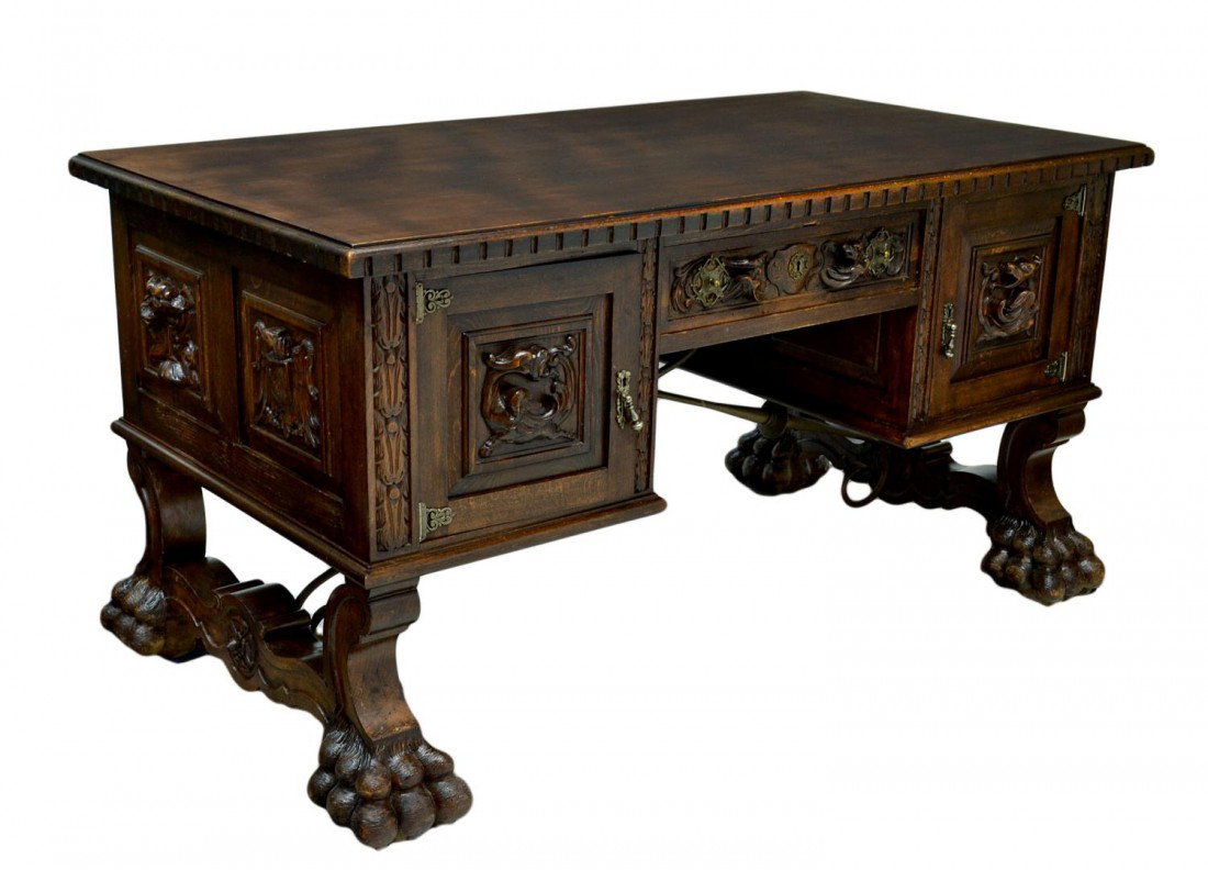 ANTIQUE SPANISH CARVED LIBRARY DESK: Spanish desk, c. 1900, rectangular carved edge top, the frieze with armorial and figural carved panels, a single drawer and two doors, one with fitted interior, resting on scroll supports with metal s