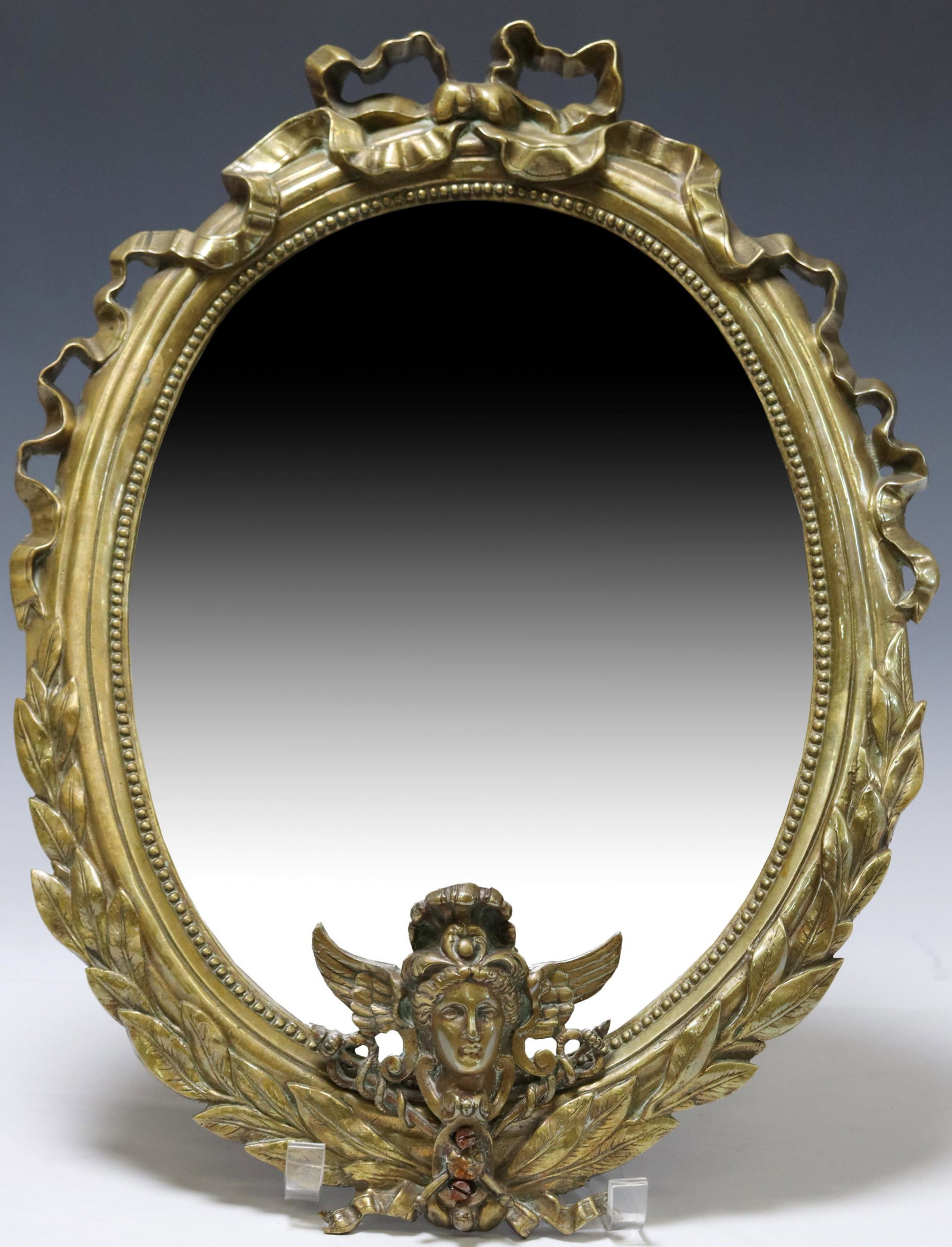 FRENCH LOUIS XVI STYLE BRONZE BEVELED WALL MIRROR: French Louis XVI style bronze wall mirror, early 20th c., having ribbon crest, over molded frame with beaded trim and figural mask motif, encasing beveled mirror plate, approx 18"h, 13.5"w, 7.4lbs Sta