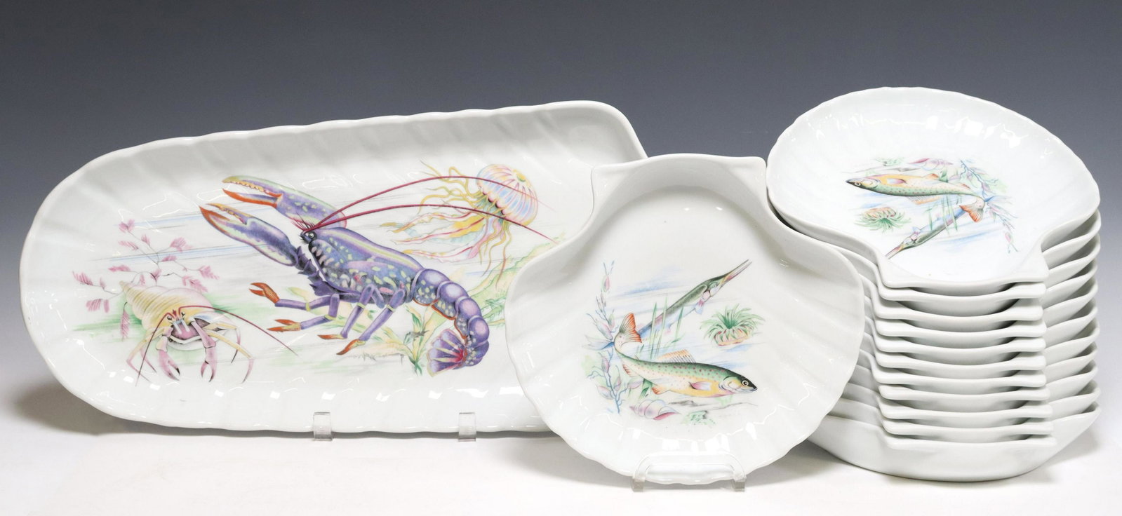 (13) FRENCH PORCELAIN FISH SERVICE: (lot of 13) French porcelain fish service, Exclusivite Les Porcelaines Monique Robert, late 20th c., including: (12) shell-shaped plates, with (six) unique transfer printed designs, approx 9"l, 10"w, 