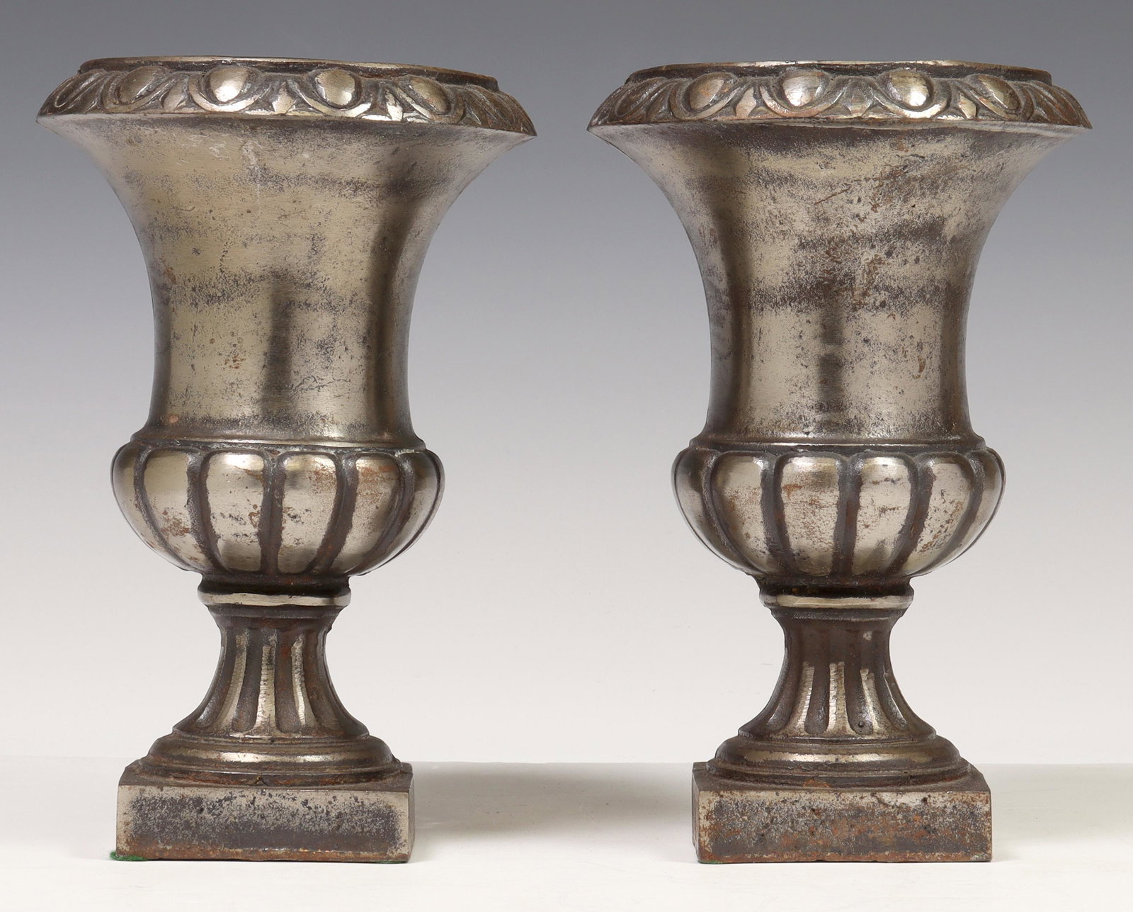 (2) NEOCLASSICAL STYLE METAL-PLATED CAST IRON URNS: (pair) Neoclassical style silver-tone metal plated cast iron urns, 20th c., each having flared rim with molded trim, over gadrooned body, rising on waisted stem, on integral platform base, approx 8"h,