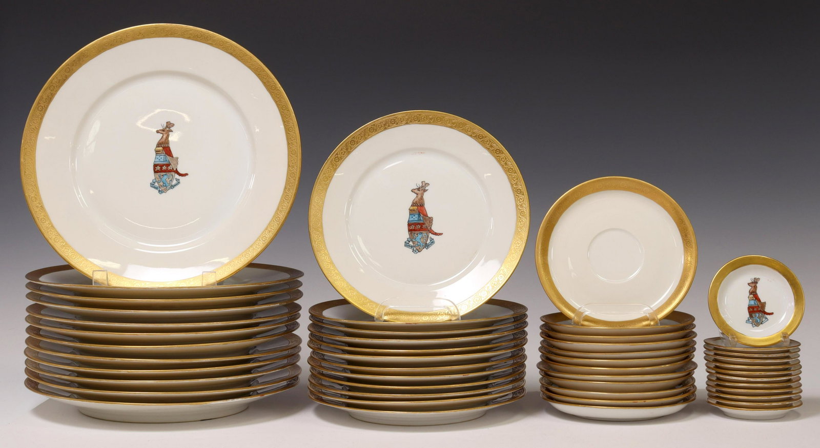 (48) MCMURRAY CREST HAND-PAINTED PORCELAIN PLATES: (lot of 48) Hand-painted porcelain partial dinner service, assembled, having parcel gilt trim, most retaining Lucie McMurray artist's signature and varied dates, with painted heraldic crest featuring 