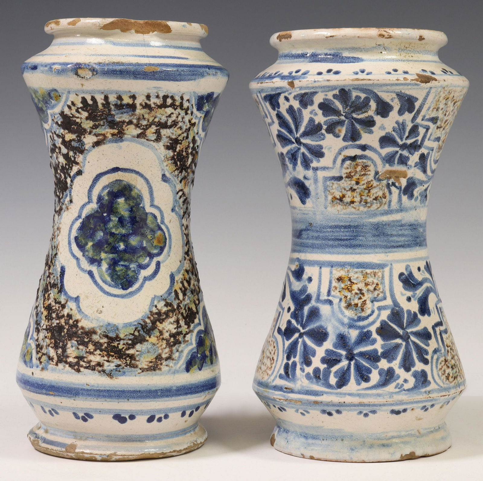 (2) TALAVERA TIN-GLAZED POTTERY APOTHECARY JARS: (lot of 2) Talavera tin-glazed earthenware albarellos/ apothecary jars, 18th c., each having flared rim, over waisted body, painted with geometric and floral motifs, typical chips, hairlines, and impe