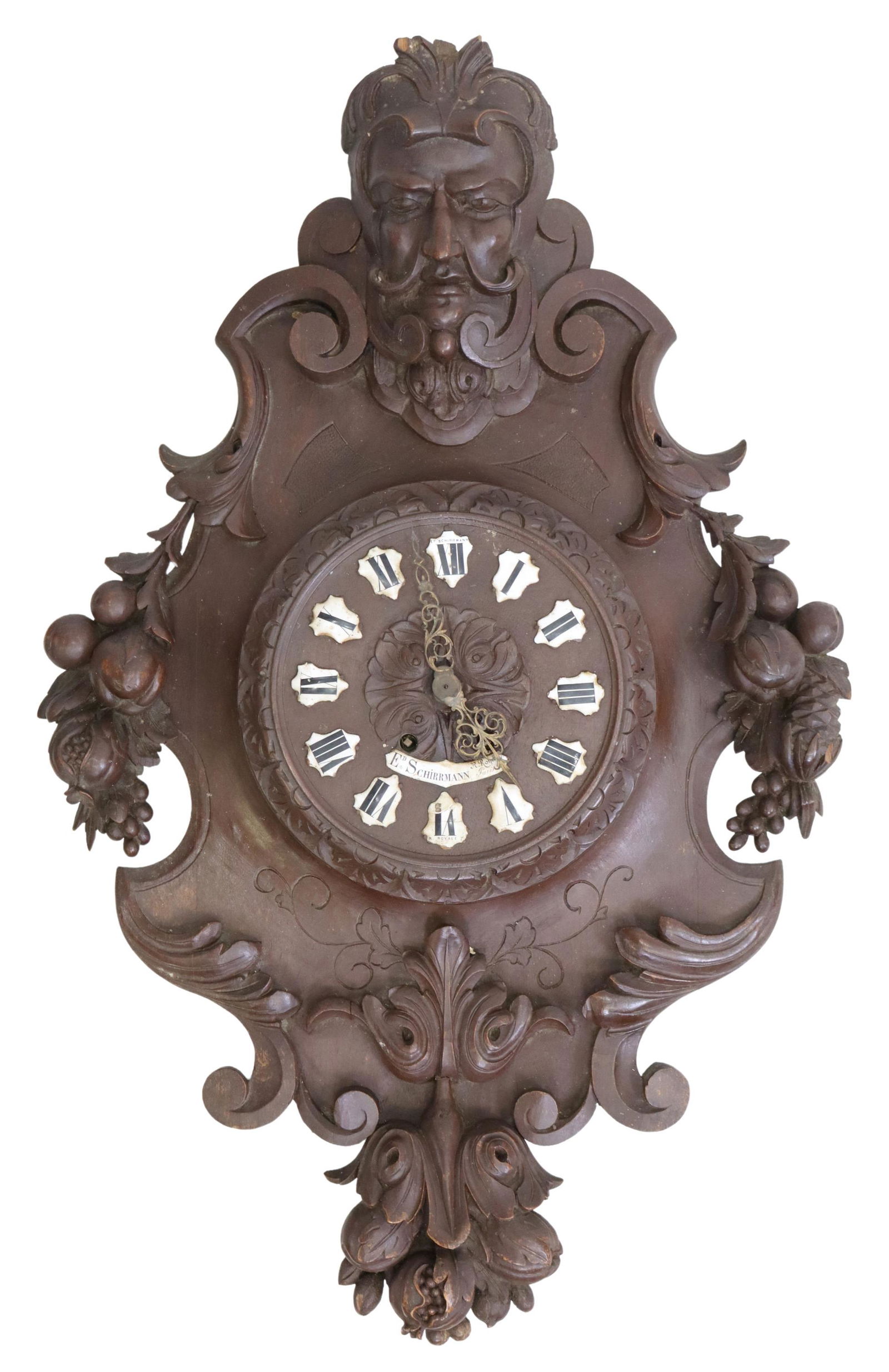 FRENCH HENRI II STYLE ED. SCHIRRMANN WALL CLOCK: French Henri II style wall-mounted clock, 19th c., figural mask crest, over shaped frame with carved fruits, centering a dial with individual enameled cartouches, black Roman numeral hour markers, tim