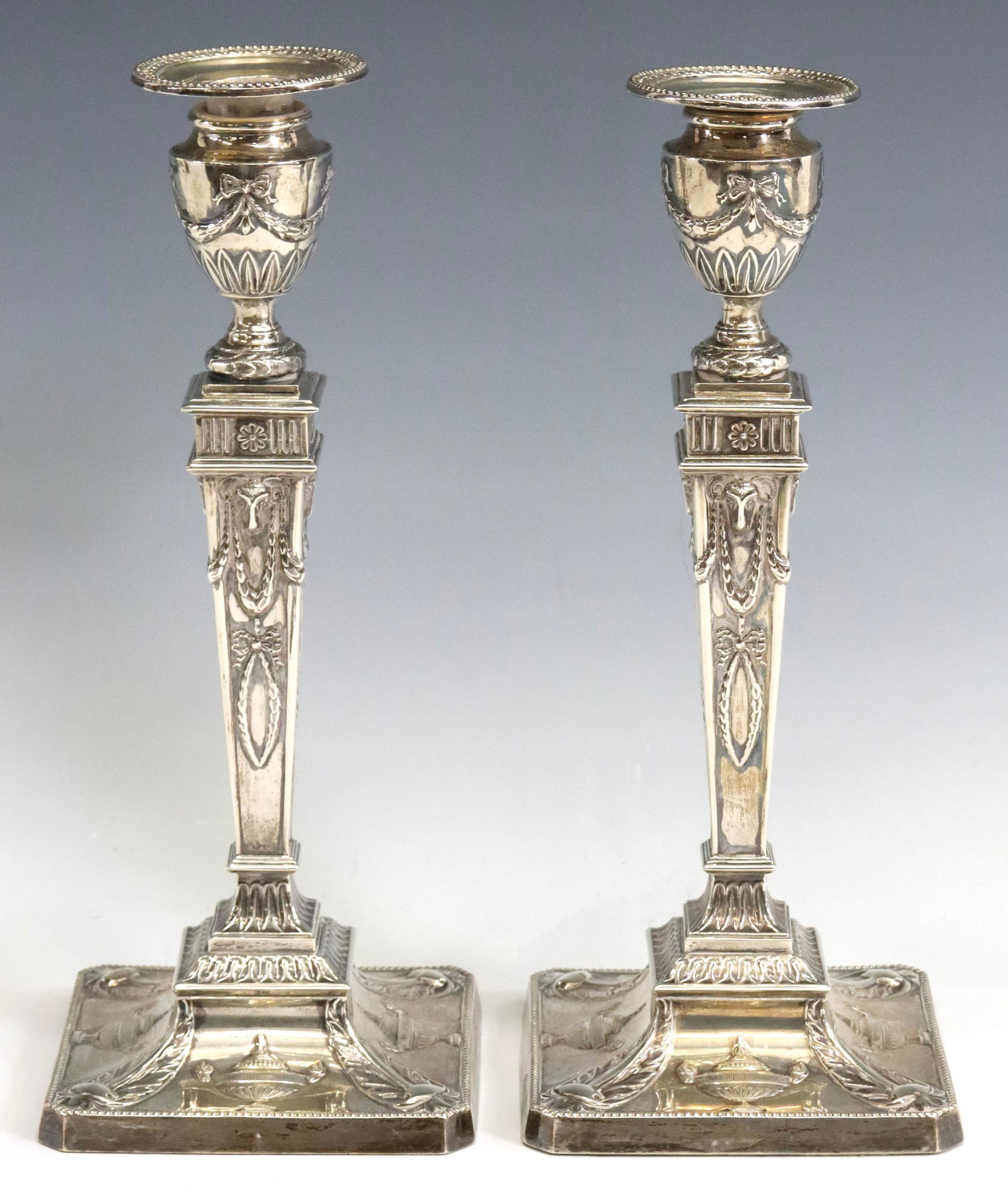 (2) ENGLISH WEIGHTED STERLING CANDLESTICKS: (pair) English Neoclassical weighted sterling silver candlesticks, Stewart Dawson & Co. Ltd., c.1907, tapered standard with rams' heads, laurel garlands, on a beaded square foot with classical urns, S