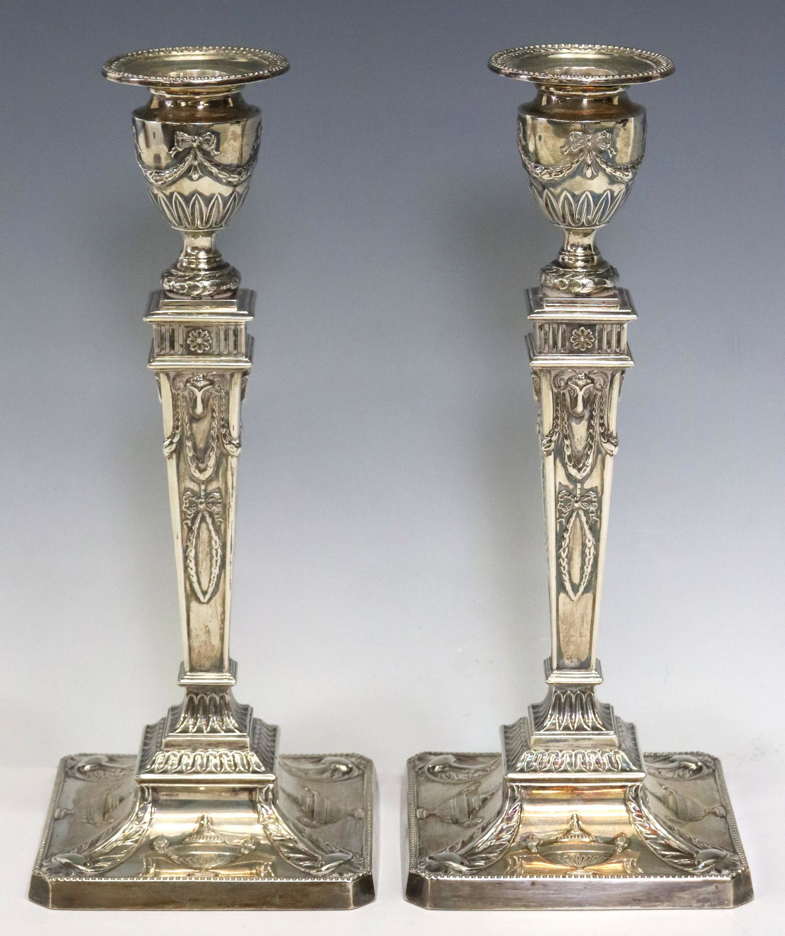 (2) ENGLISH WEIGHTED STERLING CANDLESTICKS: (pair) English Neoclassical weighted sterling silver candlesticks, Stewart Dawson & Co. Ltd., c.1907, tapered standard with rams' heads, laurel garlands, on a beaded square foot with classical urns, S
