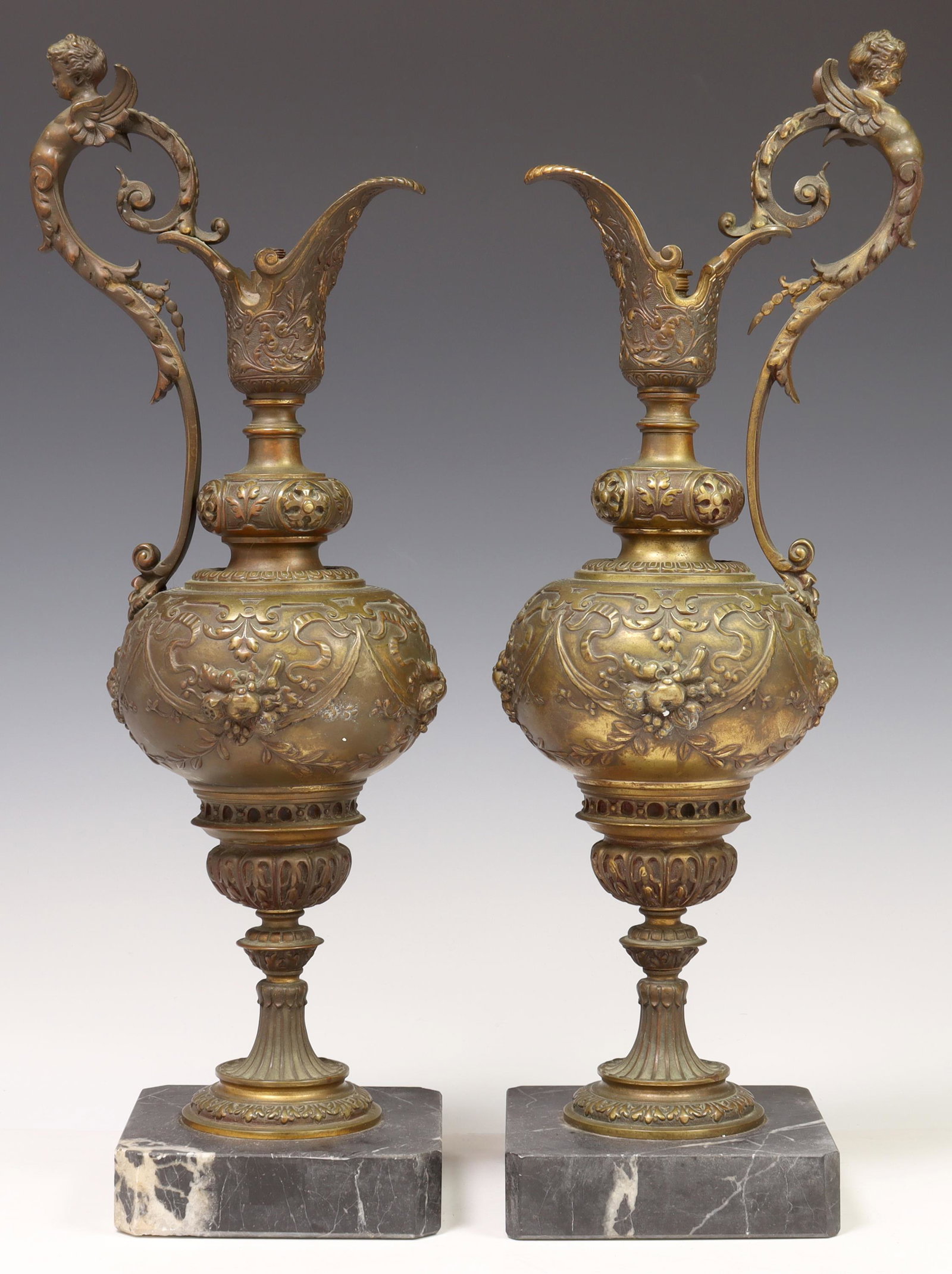 2) NEOCLASSICAL PATINATED BRONZE EWERS/ LAMP BASES: (pair) Neoclassical patinated bronze ewers, previously fashioned as table lamps, with winged cherub handle, ornamented with foliates in relief throughout, rising on canted marble base, in need of sock