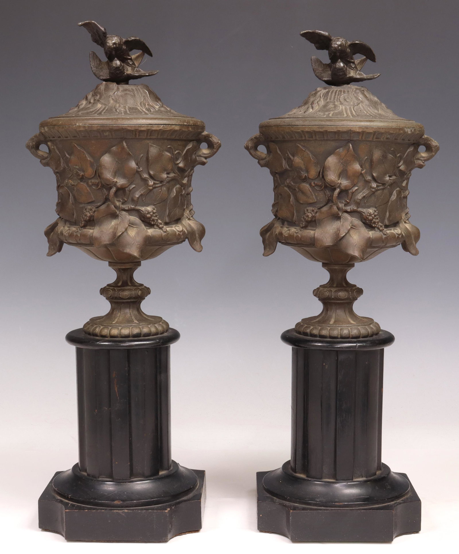 (2) PATINATED METAL URN GARNITURES: (pair) Patinated metal urns, with grapevines cast in relief, on a painted wood column, approx 14.5"h, 4.75"w, 4.75"d; 8.75lbs total Start Price: $100.00