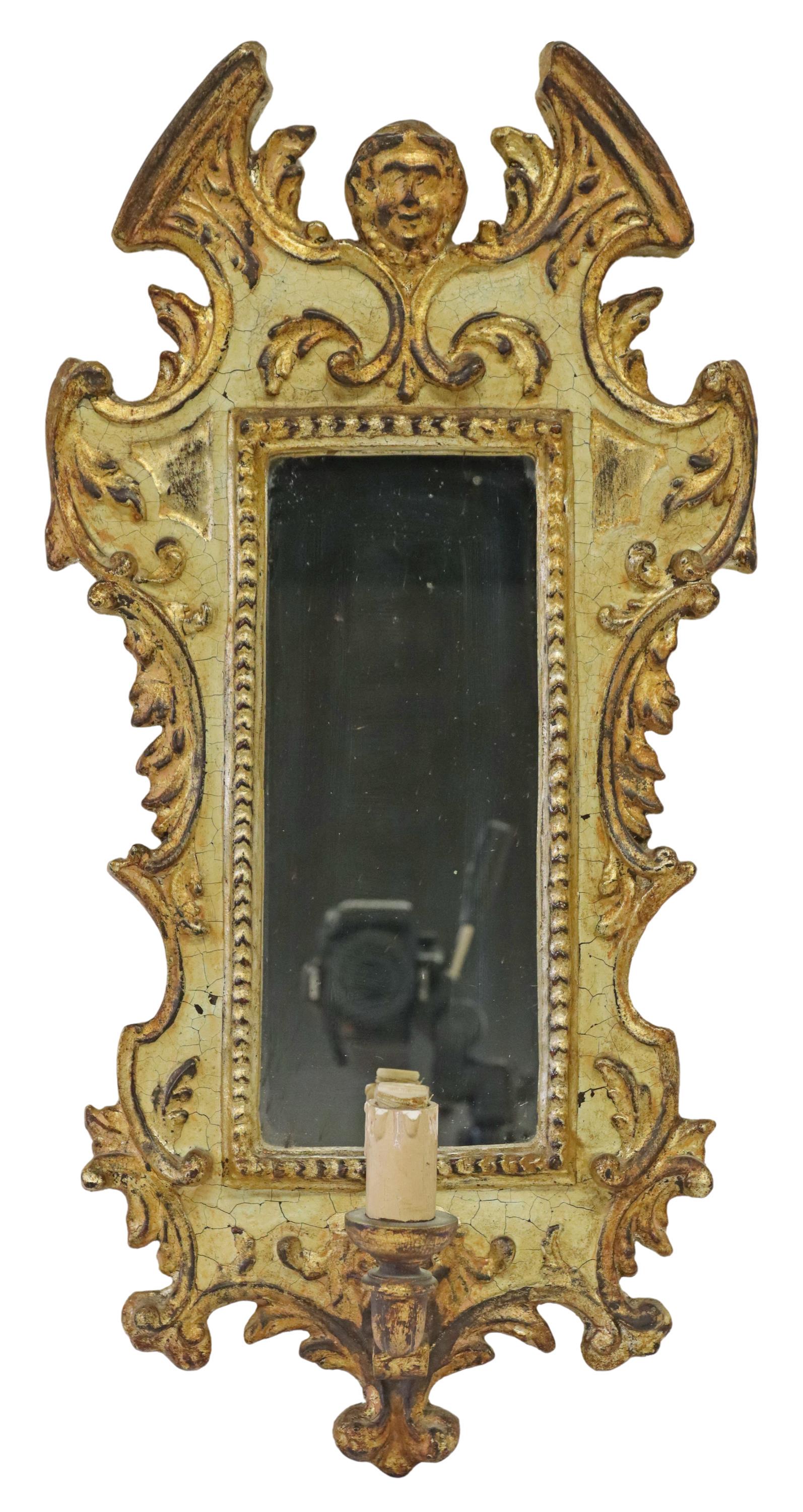 ITALIAN PARCEL GILT & PAINTED MIRRORED WALL SCONCE: Italian painted and parcel gilt mirrored wall sconce, 20th c., split pediment, centering figural mask, over foliate shaped frame, encasing flat mirror plate, above single light, in need of wiring, app