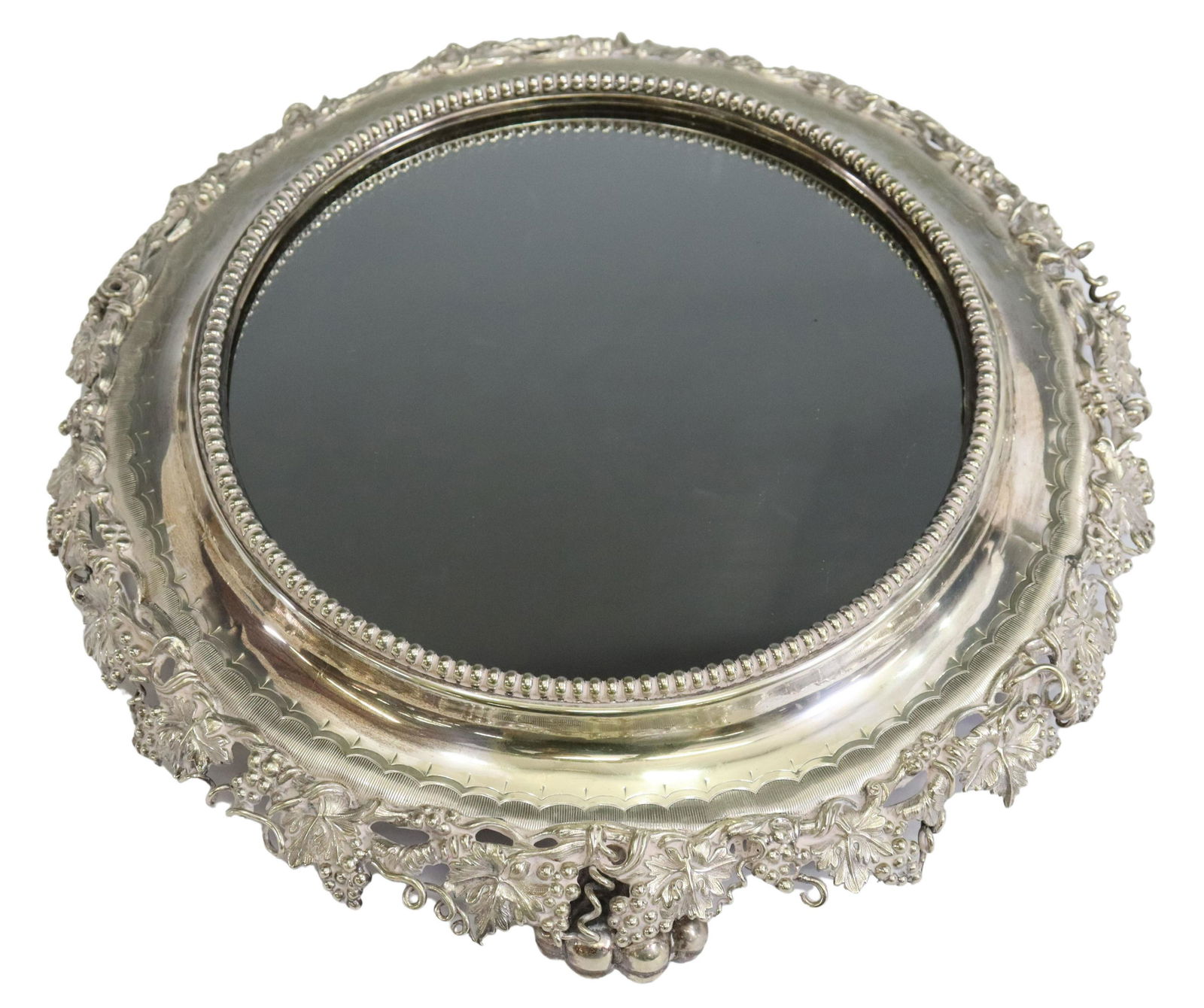 SILVERPLATE ROUND GRAPEVINE MIRROR TABLE PLATEAU: Silverplate surtout de table/ table plateau, round form with interior beaded trim, encasing flat mirror plate, over pierced grapevines, ending on grape cluster feet, approx 3"h, 15.25"diam, 5.5lbs for