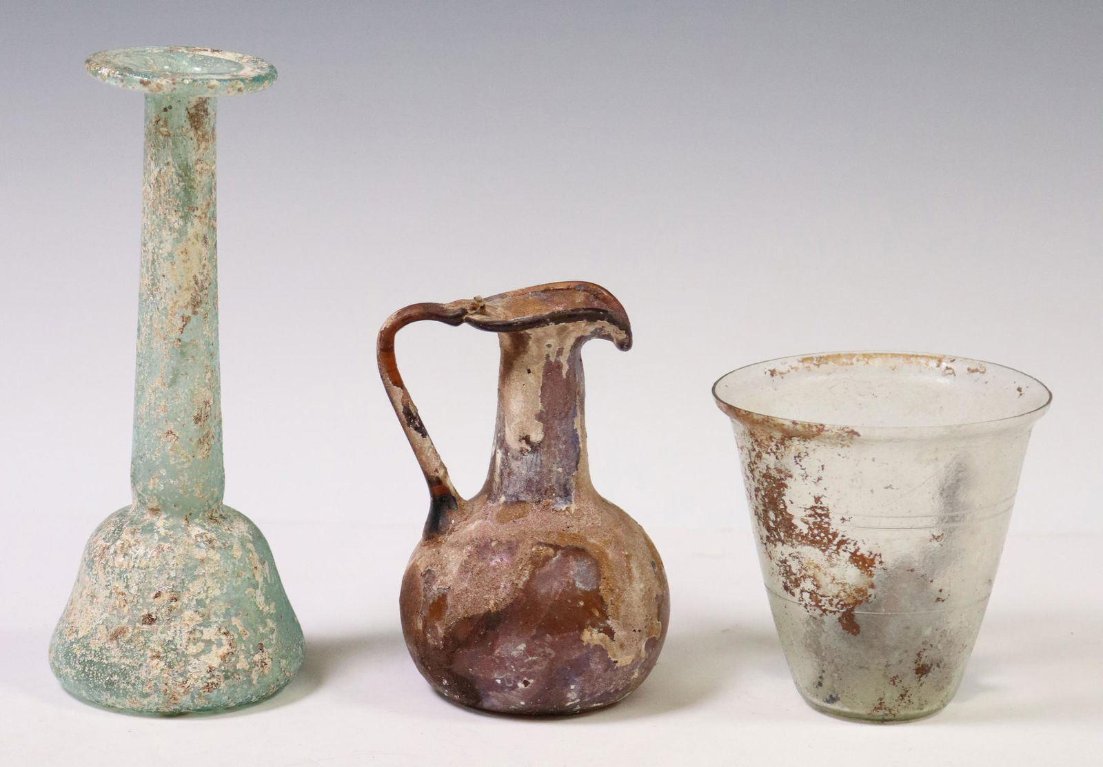 (3) ROMAN STYLE GLASS BEAKER, EWER & BOTTLE: (lot of 3) Roman style iridescent glass vessels, including: (1) beaker with engraved horizontal bands, approx 3.25"h, 3 3/8"diam, (1) small handled ewer, approx 4.25"h, (1) bottle/ flask, approx 6.5"h