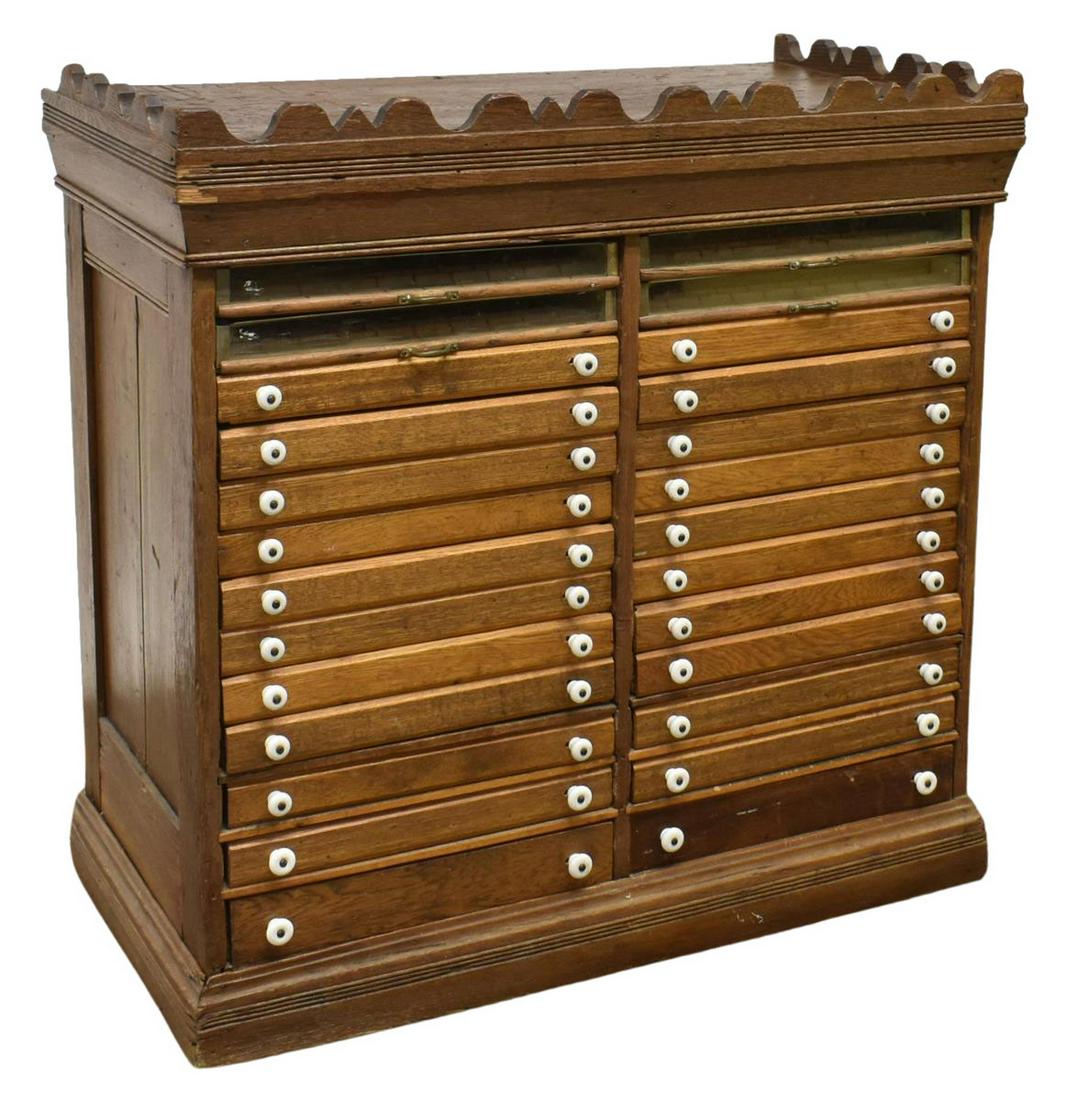 AMERICAN GENERAL STORE OAK SPOOL CABINET: American oak spool cabinet, c.1900s, four glazed drawers, over twenty-two drawers with porcelain pulls, rising on a plinth base, separation to side panels, losses to crown molding, approx 36.5"h, 36.5