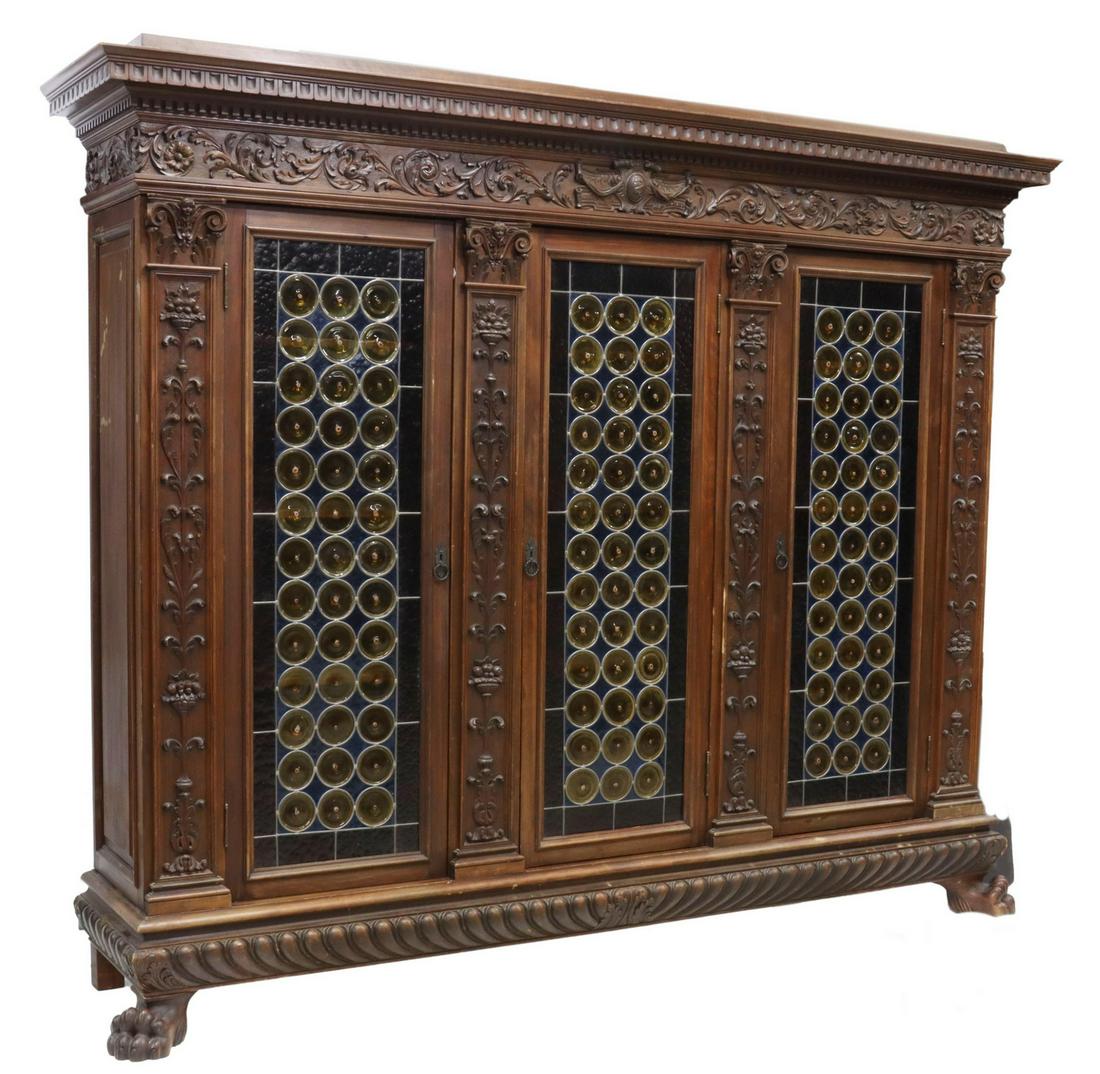 ITALIAN RENAISSANCE REVIVAL CARVED WALNUT BOOKCASE: Italian Renaissance Revival carved walnut bookcase, early 20th c., molded cornice, panels with running foliate ornamentation, fitted with three cabinet doors with leaded bullseye glass, opening to int