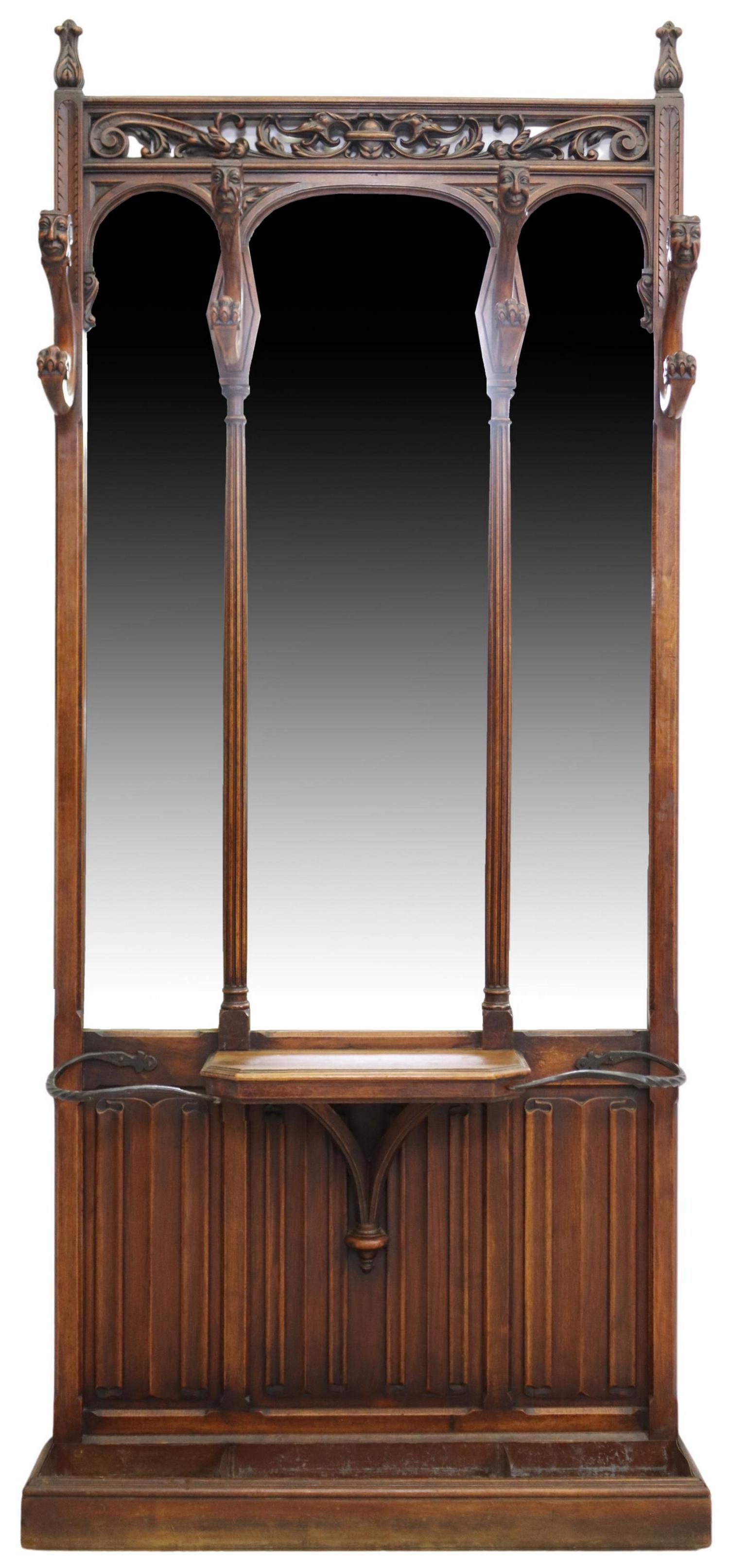FRENCH GOTHIC REVIVAL CARVED WALNUT HALL STAND: French Gothic Revival walnut hall tree, late 19th c., carved and pierced frieze, four hooks with masks, arched mirror plate, small shelf, linenfold back panel, wrought iron railing, over inset metal t