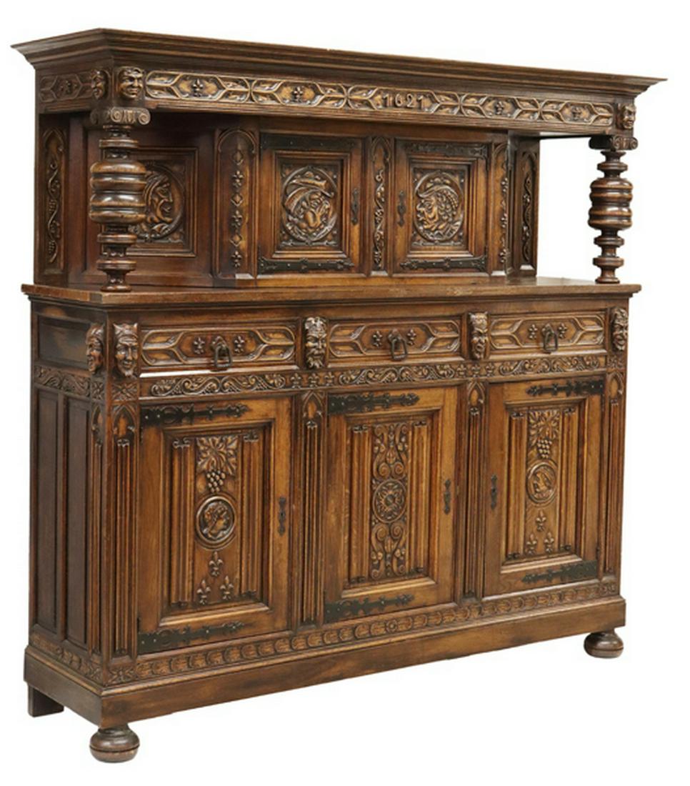 FRENCH FIGURAL CARVED OAK COURT CUPBOARD: French carved oak court cupboard, 19th c., the whole carved with figural masks, having molded cornice, two top cabinets, flanked by large turned supports, over lower case fitted with three drawers, an