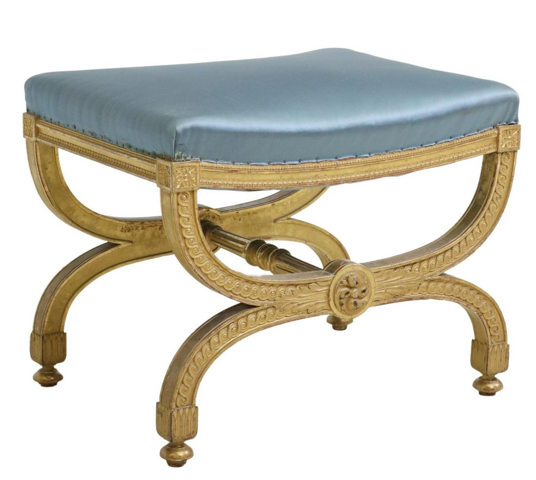 NEOCLASSICAL STYLE GILTWOOD UPHOLSTERED FOOTSTOOL: Neoclassical style giltwood footstool/ ottoman, 20th c., having upholstered seat, over curule frame, with foliates and running ornamentation, fluted center stretcher, ending on bun feet, approx 19.5"h