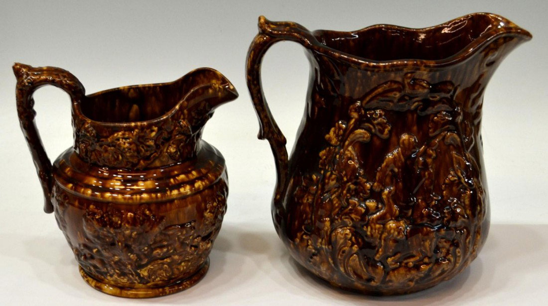 (2) LARGE POTTERY PITCHERS IN A ROCKINGHAM GLAZE: (lot of 2) Rockingham glaze pottery pitchers: (1) showing figural hunt scene in relief, 9.75"h; (1) marked obscurely underfoot, showing a hound and stag hunt scene in relief, chip at handle, 8"h; 7.75