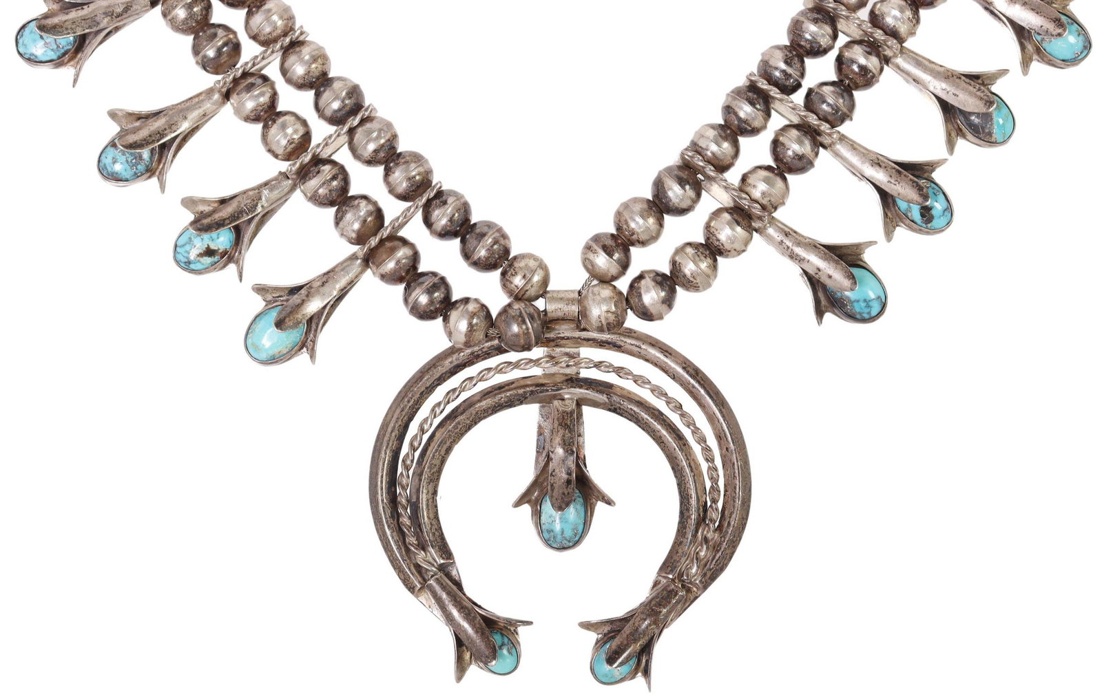 NATIVE AMERICAN TURQUOISE SQUASH BLOSSOM NECKLACE: Native American silver (content unknown) squash blossom necklace, sixteen blossoms each set with a turquoise cabochon, central naja pendant also set with turquoise, double bench bead strands, ending i