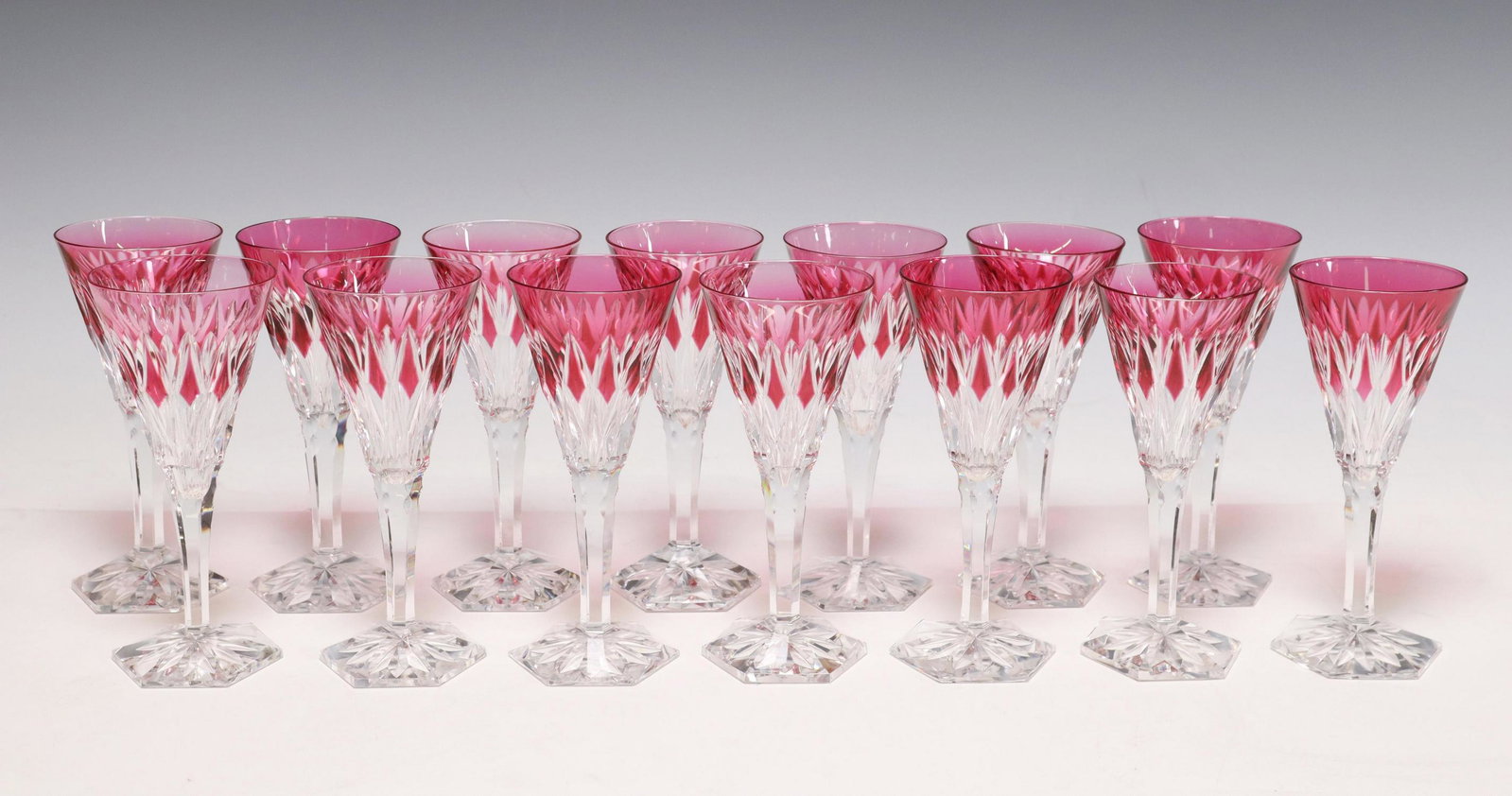 (14) VAL ST. LAMBERT 'HAFNIA FANTAISIE' WINE STEMS: (lot of 14) Val St. Lambert cranberry cut to clear crystal wine stems, in the "Hafnia Cut Fantaisie" pattern, with fan and star motifs, unsigned, two with minute chips to base, approx 6.25"h, 2.75"dia