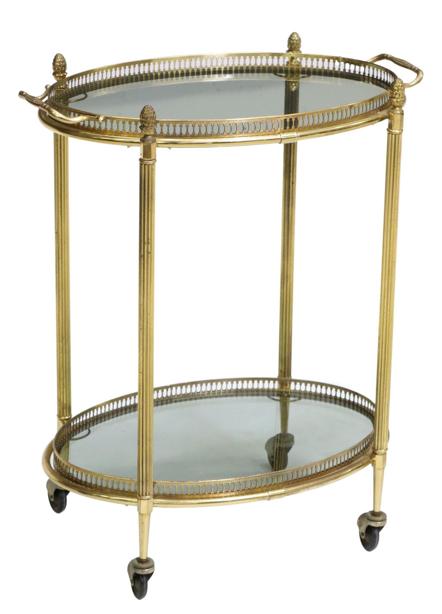 ITALIAN 2-TIER GILT METAL & SMOKED GLASS BAR CART: Italian gilt metal and glass bar cart/ service trolley, 20th c., having removable tray top, pierced gallery framing two ovular smoked glass tiers, rising on fluted supports, ending on castors, approx 