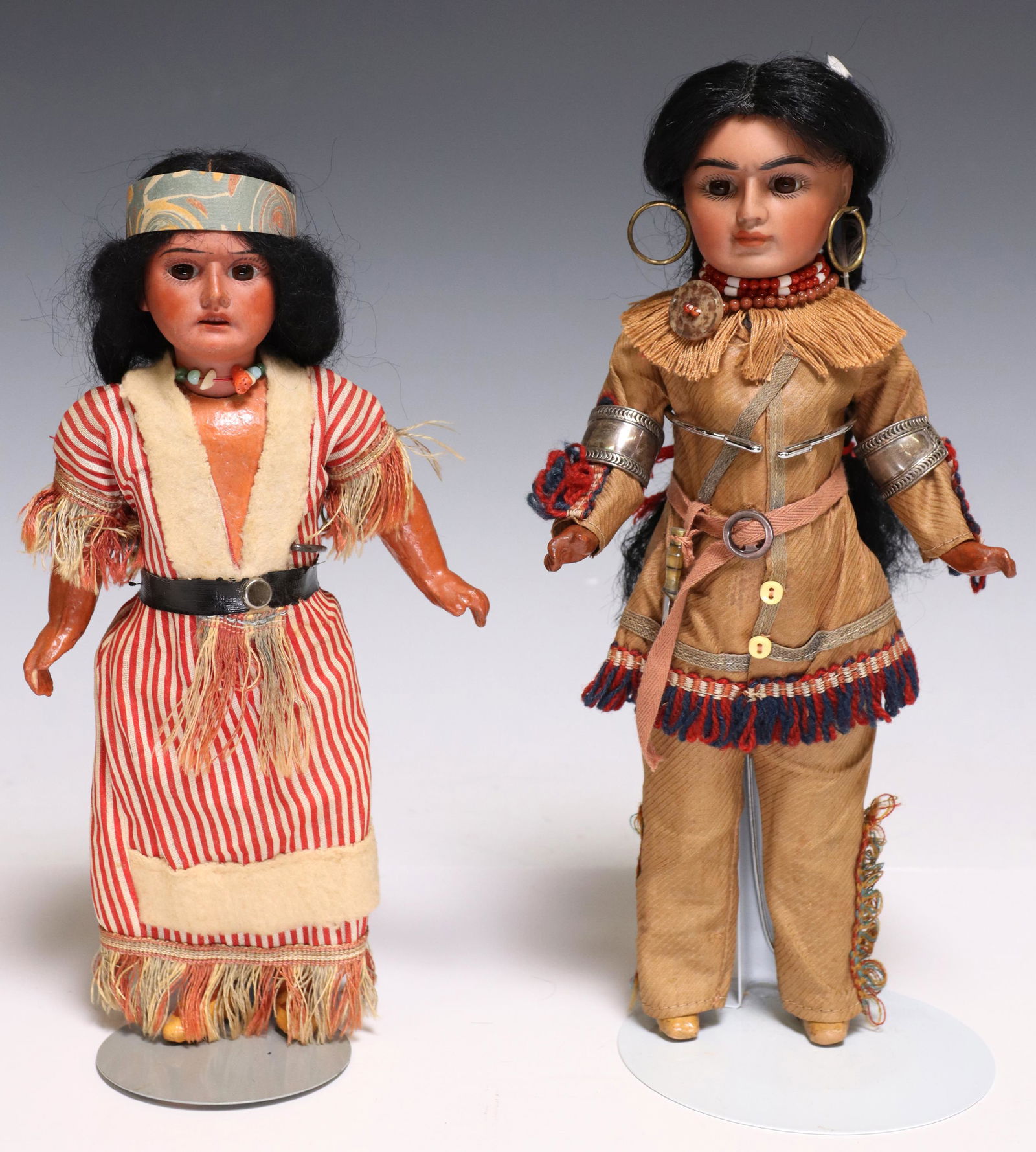 (2) ARMAND MARSEILLE & OTHER NATIVE AMERICAN DOLLS: (lot of 2) Bisque head dolls, each modeled as a Native American, painted bisque face with inset glass eyes, jointed composition body, dressed in fringed garments, accompanied by fitted display stand,