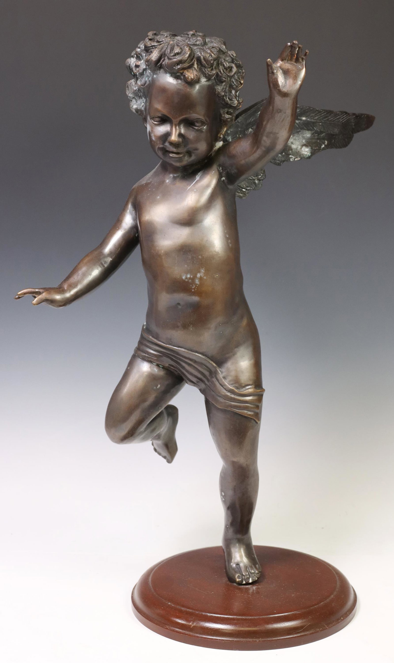 PATINATED BRONZE FIGURAL WINGED CHERUB SCULPTURE: Patinated bronze figural sculpture, Winged Cherub, in dynamic standing pose, on circular wood base, approx 24"h, 14"w, 14"d, 17lbs **Provenance: From a fine Texas estate** Start Price: $100.00