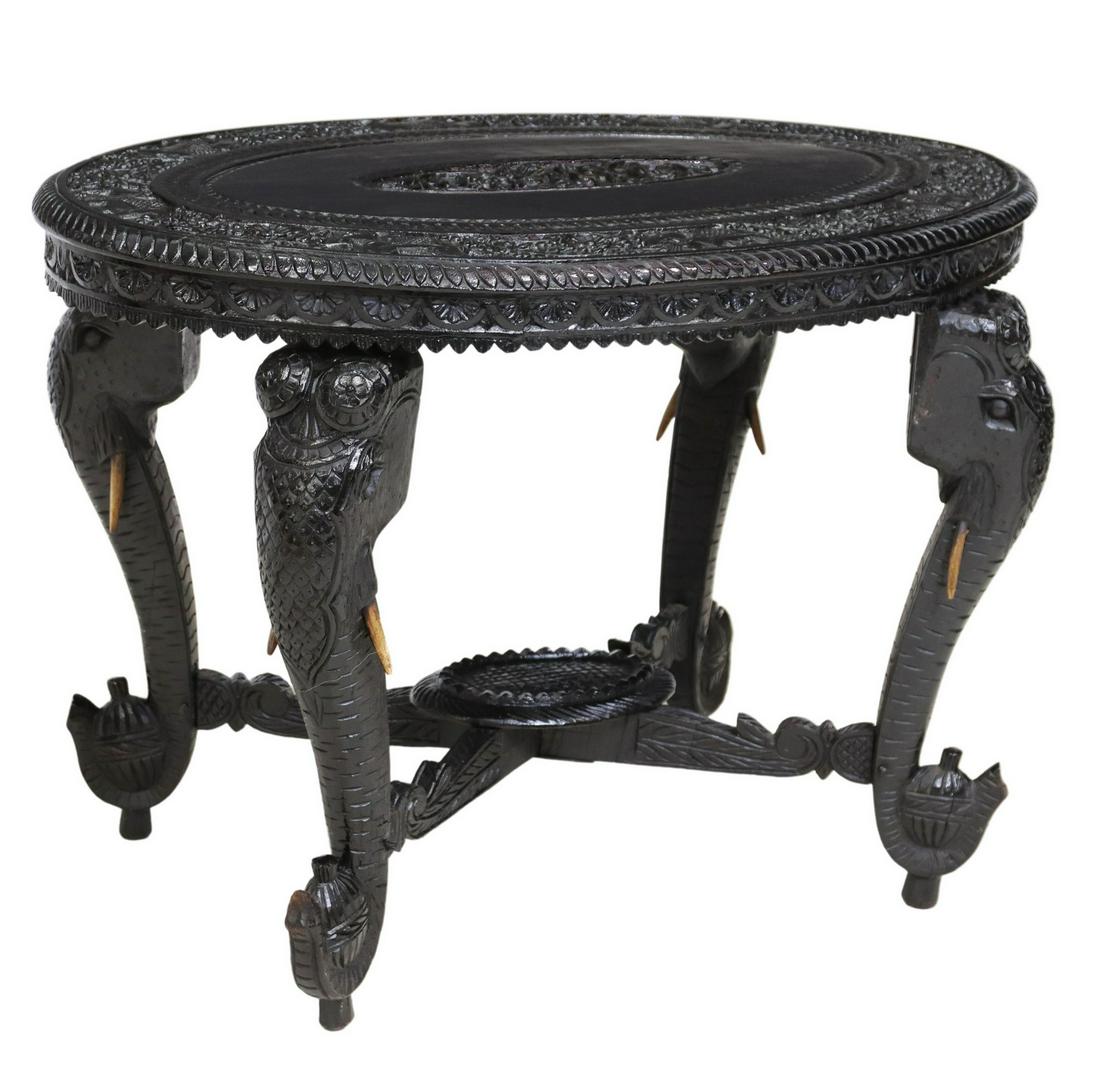 CARVED ELEPHANT-LEG OCCASIONAL TABLE, INDIA: Carved wood occasional table, India, 20th c., in a black painted finish, having ovular top with carved elephants, floral motifs, foliate scrollwork, rising on elephant-form supports, joined by cross s