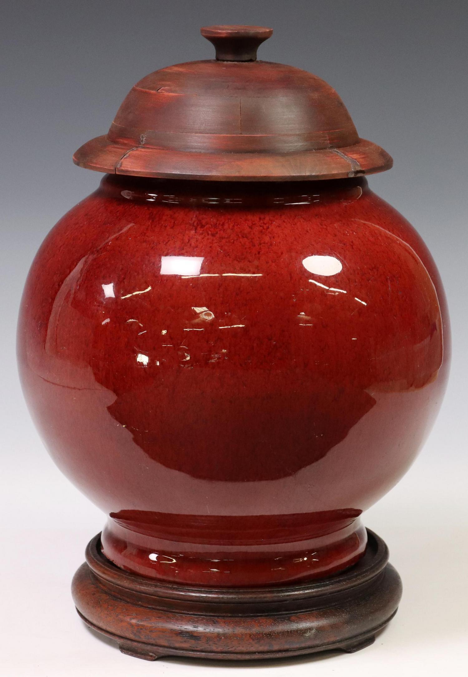 CHINESE SANG DE BOEUF PORCELAIN JAR ON STAND: Chinese sang de boeuf (oxblood) porcelain lidded jar, with later wood lid and stand, reduced neck, intact with star fracture, small chips underfoot, approx 13.5"h (overall), 11.75"h (jar), 9"diam, 8lb