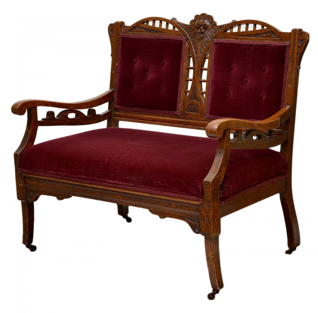 VICTOIAN OAK FRAMED SETTEE, CARVED GREEN MAN: American Victorian Eastlake oak framed settee, c. 1890, having a central carved crest depicting a Green Man flanked, buttoned red upholstered back panels over red upholstered seat, arms with reticulat
