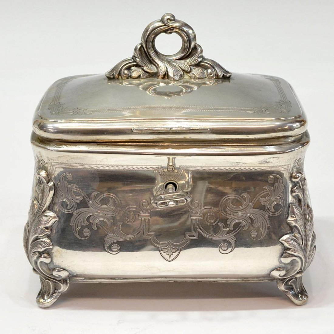 CONTINENTAL 750 SILVER ENGRAVED CASKET: Continental 750 silver casket of rectangular form, the hinged lid with foliated knop opening to interior in a gilt wash, engraved motifs on the exterior rise on four acanthus supports, retaining key, 