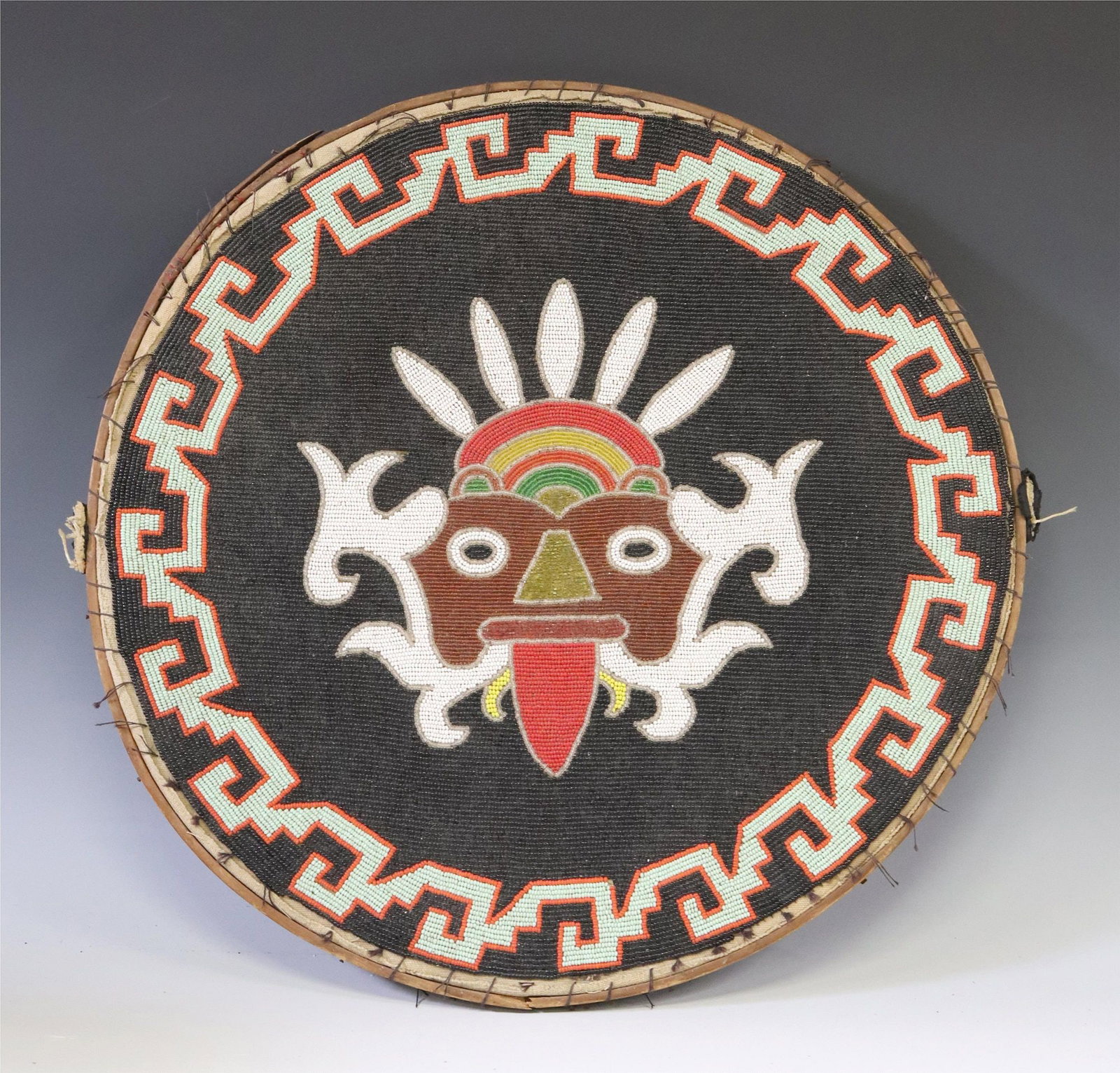 AZTEC TLALOC CHAQUIRA BEADED PARADE SHIELD: Aztec beaded parade shield, Mexico, early 20th c., chaquira beads, on wood frame, depicting Tlaloc rain god, leather handle to back, approx 18.5"diam, 2lbs Start Price: $80.00