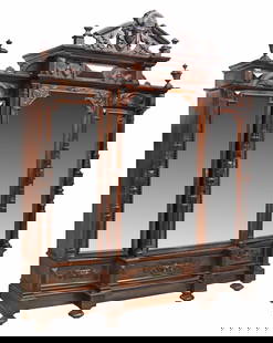 VICTORIAN CARVED MIRRORED THREE-DOOR ARMOIRE: Victorian mirrored armoire, late 19th/ early 20th c., contrasting accents in dark finish, having split pediment crest, centering figural mask, three beveled mirror doors, flanked by foliate carved and