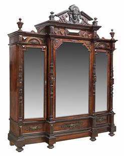 VICTORIAN CARVED MIRRORED THREE-DOOR ARMOIRE: Victorian mirrored armoire, late 19th/ early 20th c., contrasting accents in dark finish, having split pediment crest, centering figural mask, three beveled mirror doors, flanked by foliate carved and