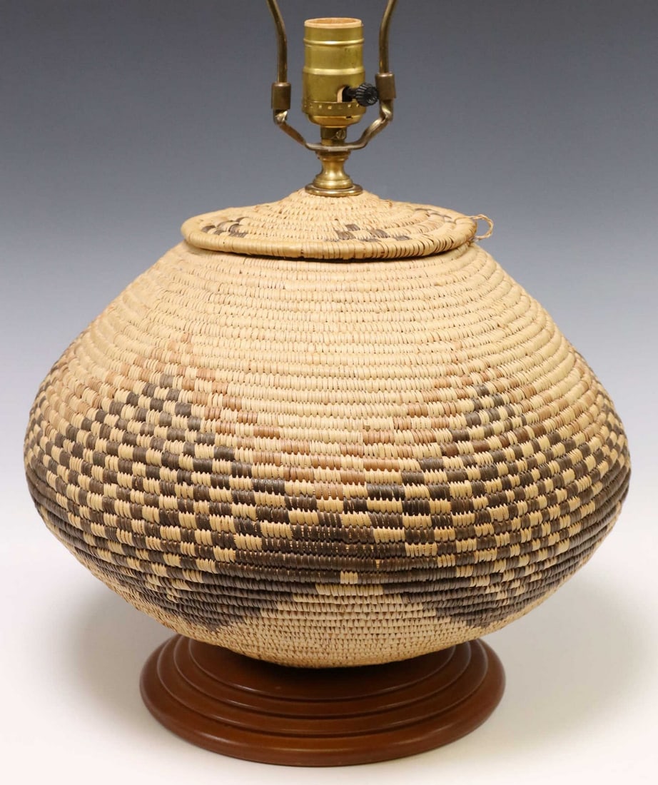 WOVEN BASKET ONE-LIGHT TABLE LAMP WITH SHADE: Woven basket, now fashioned as a single-light table lamp, with geometric diamond pattern, rising on circular foot, accompanied by black fabric shade, observed operating, overall: approx 21"h, 14"w, 13