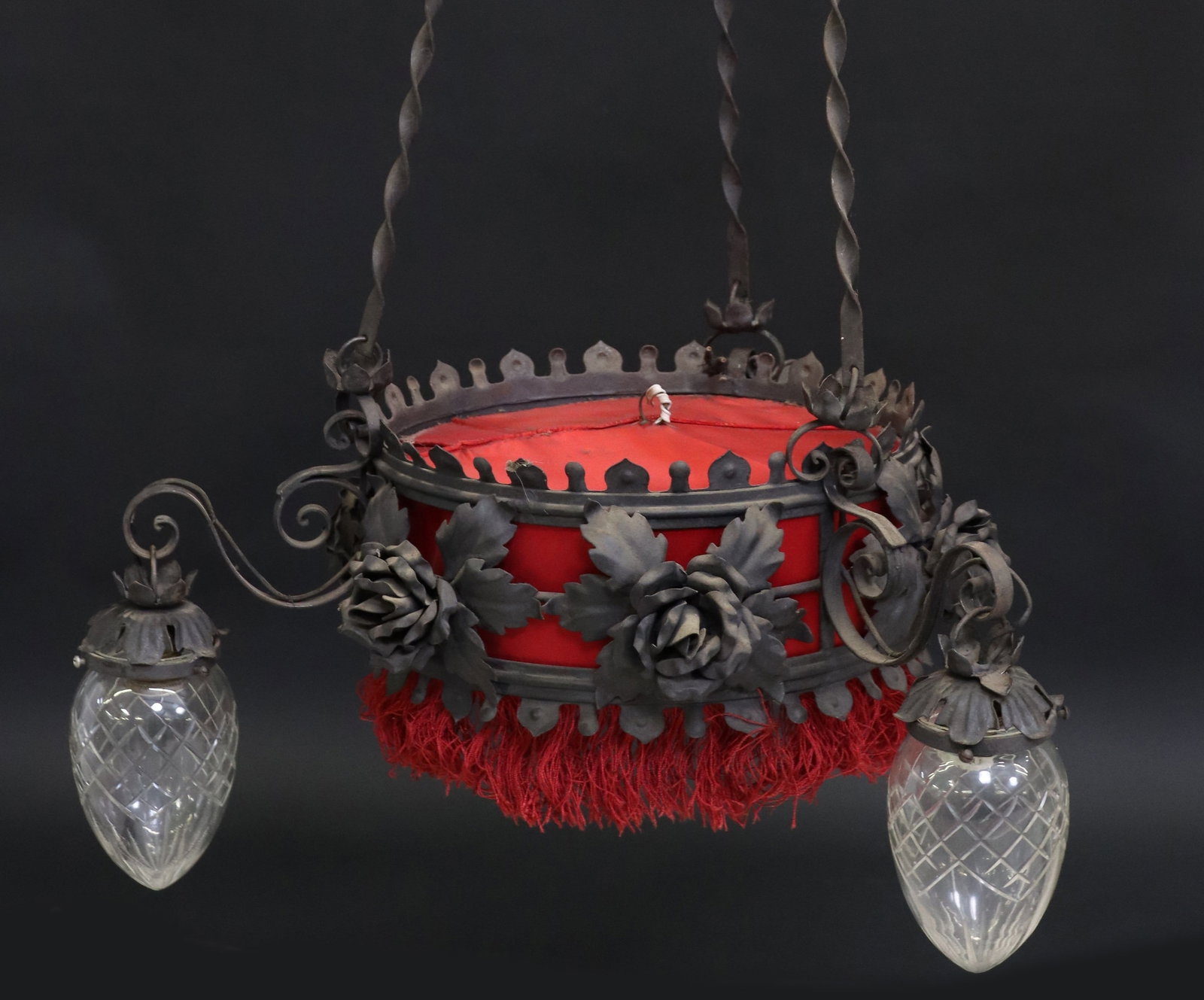 BAROQUE STYLE WROUGHT IRON FOUR-LIGHT CHANDELIER: Baroque style wrought iron four-light chandelier, early 20th c., having circular frame with foliate and floral motifs, red fabric shade terminating on fringed trim, concealing single light, three scro