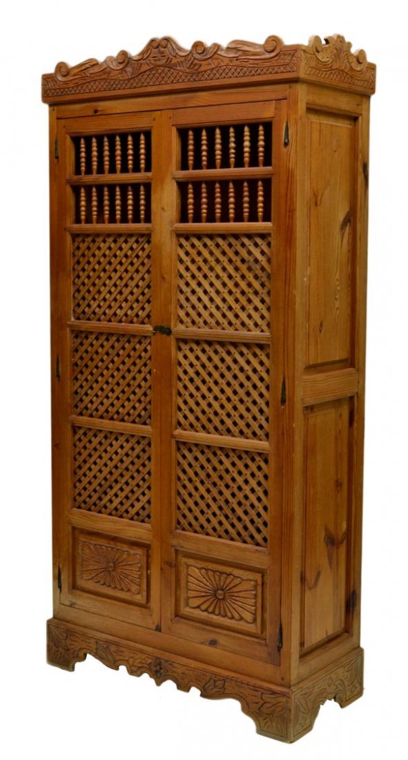 SPANISH PINE LINEN CABINET: Spanish longleaf linen cabinet, Barcelona, first half 20th c., a shaped carved crest over two lattice faced doors with spindles and carved lower panels opening to interior shelves, raised side panels,