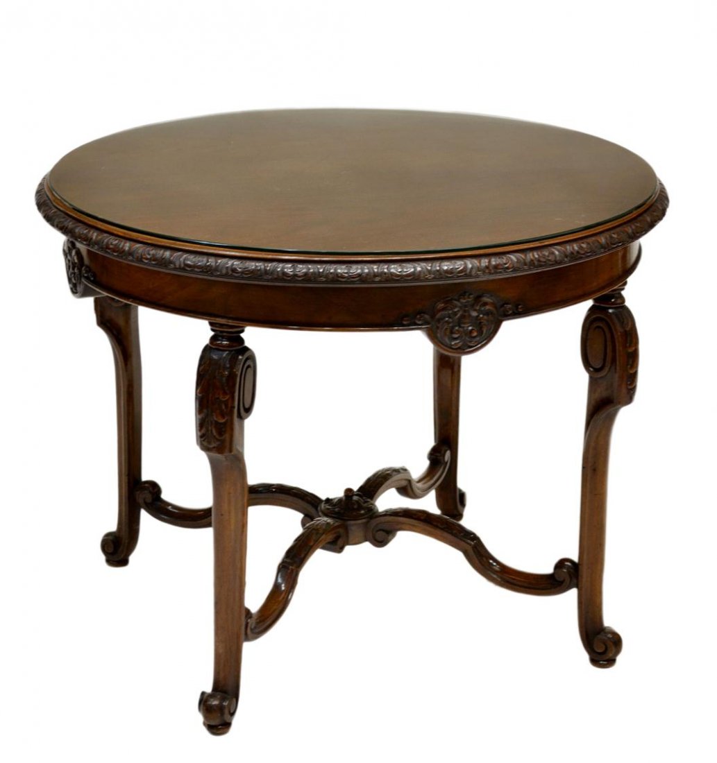 ROUND WALNUT FINISH COFFEE TABLE: Round walnut finish coffee table, Spain, 20th c., added protective glass top, set on straight legs joined by shaped stretcher with foliate carved accents, scrolled feet, 24"h, 31.5"d Start Price: $100