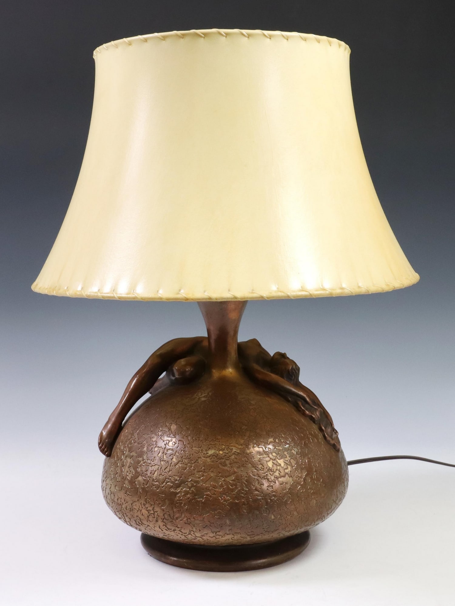 OLIVE KOOKEN ART DECO FEMALE NUDE 2-LT TABLE LAMP: Art Deco copper-clad ceramic two-light table lamp, Olive Kooken, bulbous textured base with reclining female nude, signed underfoot, accompanied by hide shade, observed operating for five minutes, lam