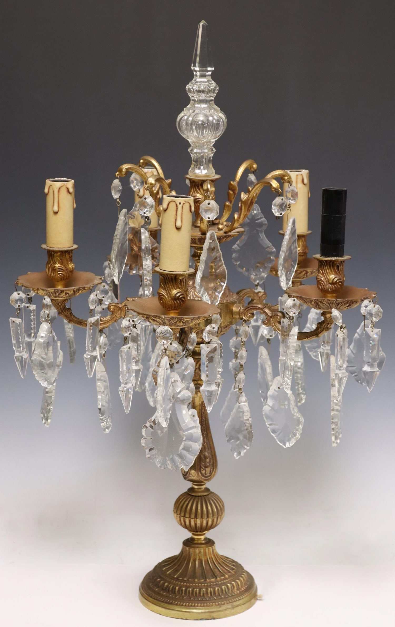 FRENCH GILT METAL & CRYSTAL FIVE-LIGHT GIRANDOLE: French gilt metal and crystal five-light girandole, 20th c., electrified, colorless shaped glass finial, baluster standard issuing scrolled arms, ending in molded bobeches and faux candles, in need of
