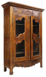 FRENCH PROVINCIAL CARVED WALNUT ARMOIRE: French Provincial carved walnut armoire/ display cabinet, early 19th c., having stepped cornice, over dual glazed cabinet doors, carved with scrolled foliates and floral motifs, opening to adjustable-