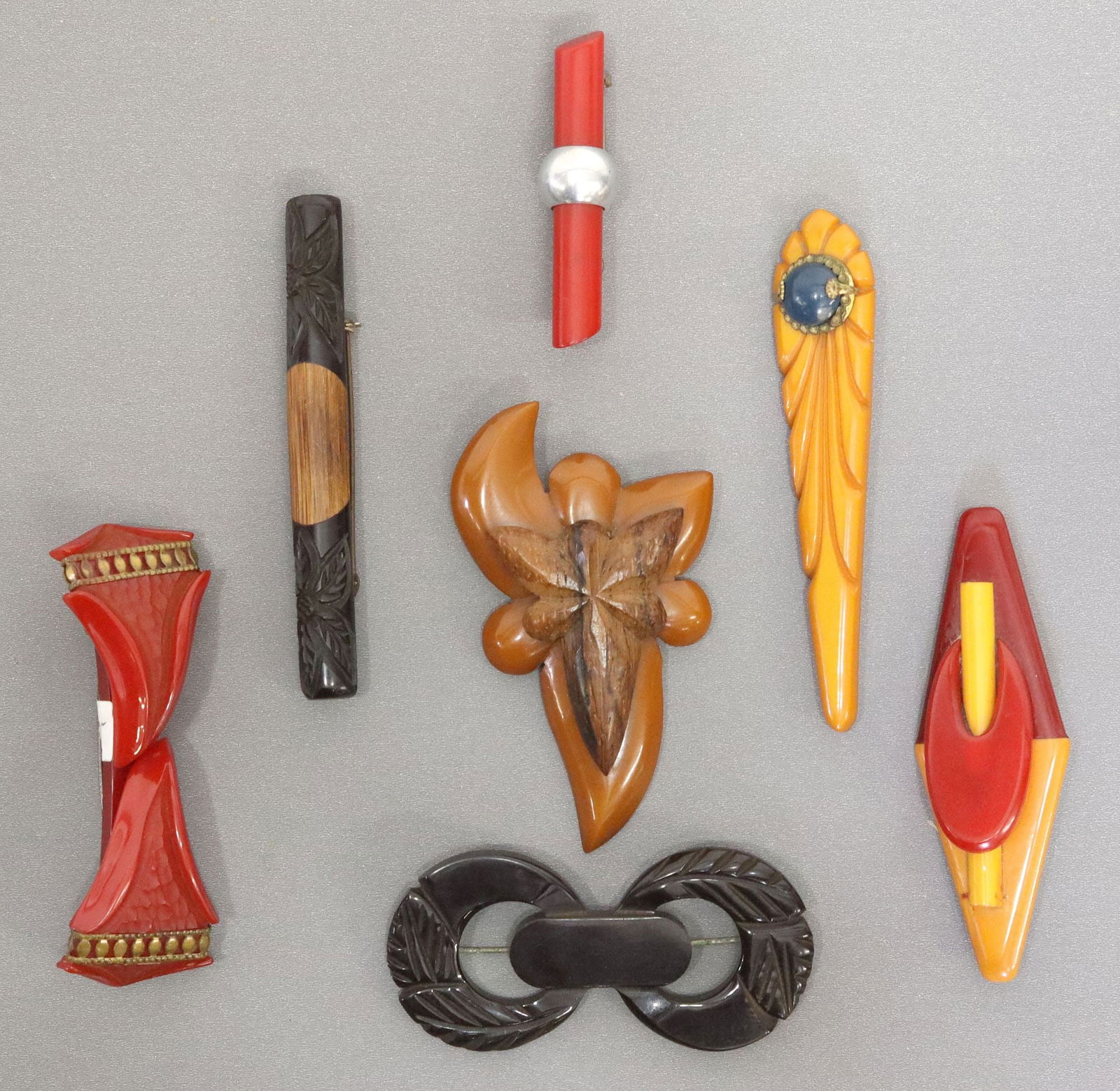 (7) VINTAGE CARVED BAKELITE & OTHER MATERIAL BROOCHES: (lot of 7) Vintage Bakelite with other material brooches, including: (1) toffee floriform mounted with carved wood, (1) flanked triangular shapes with channeling and mounted gilt metal trim, (1) butte