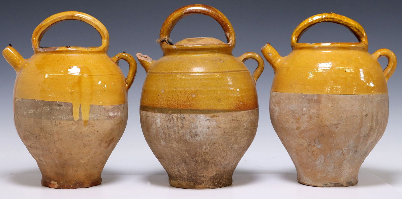 (3) FRENCH YELLOW-GLAZED EARTHENWARE WATER JUGS: (lot of 3) French Provincial earthenware water jugs, with ochre-colored glazed rim, having top and side handles, over tapered body, typical glaze loss and chips, one with retaining lid, one