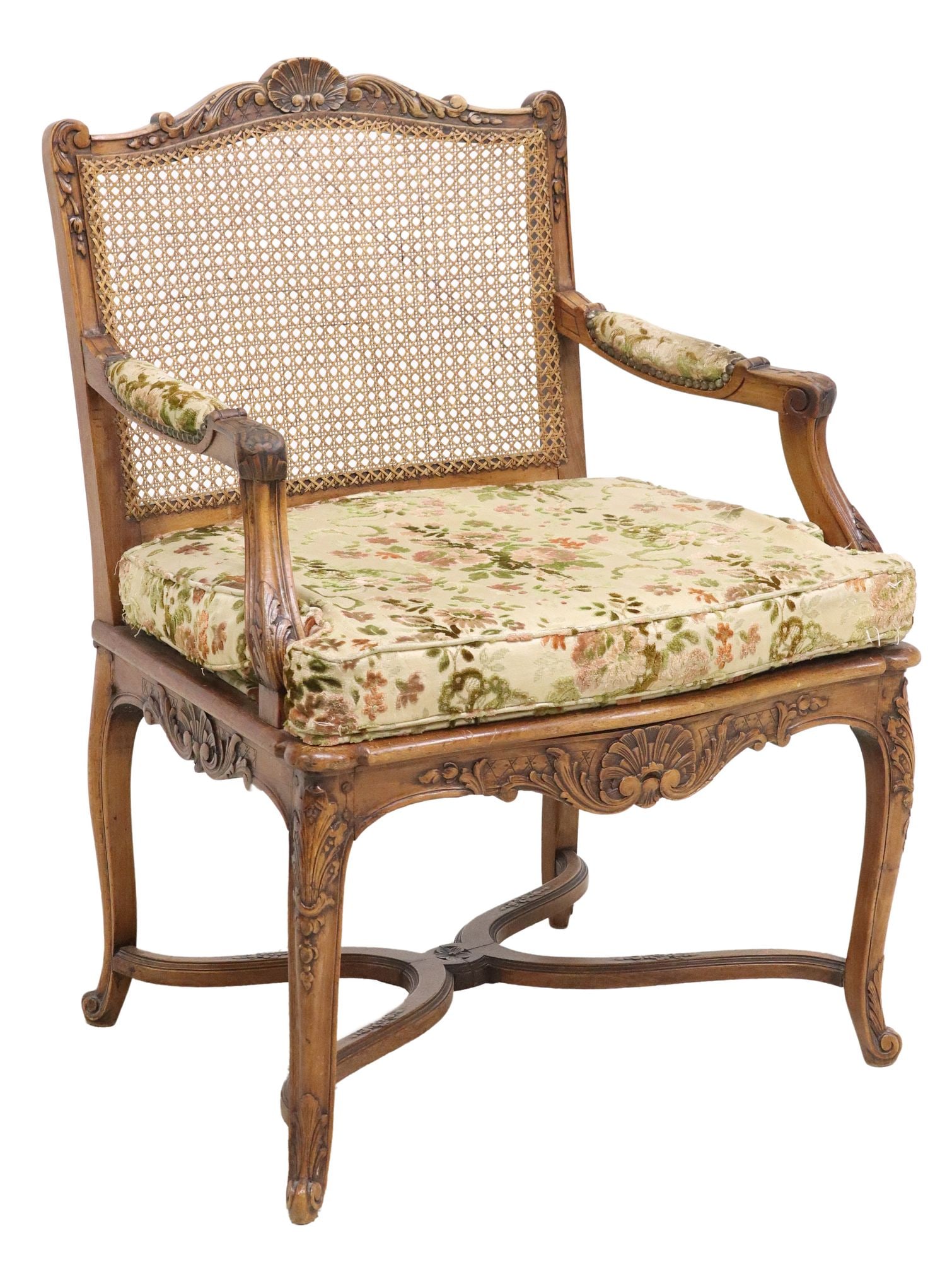 FRENCH LOUIS XV STYLE CARVED WALNUT & CANED FAUTEUIL: French Louis XV style carved walnut armchair, early 20th c., having fanned shell crest, over caned back, padded arms and removable seat cushion in floral patterned upholstery, rising on stretcher-join
