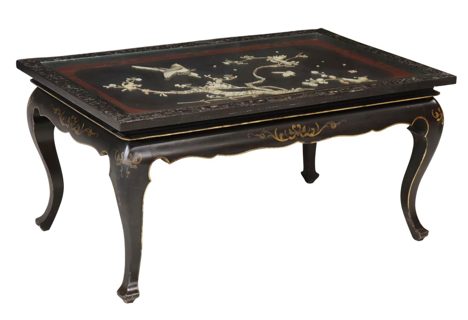 JAPANESE MOP INLAID BLACK LACQUER COFFEE TABLE: Japanese black lacquered coffee table, 20th c., having inset and applied bone and mother-of-pearl birds and trees, under glass top, table with carved floral border, over scalloped apron, rising on cab
