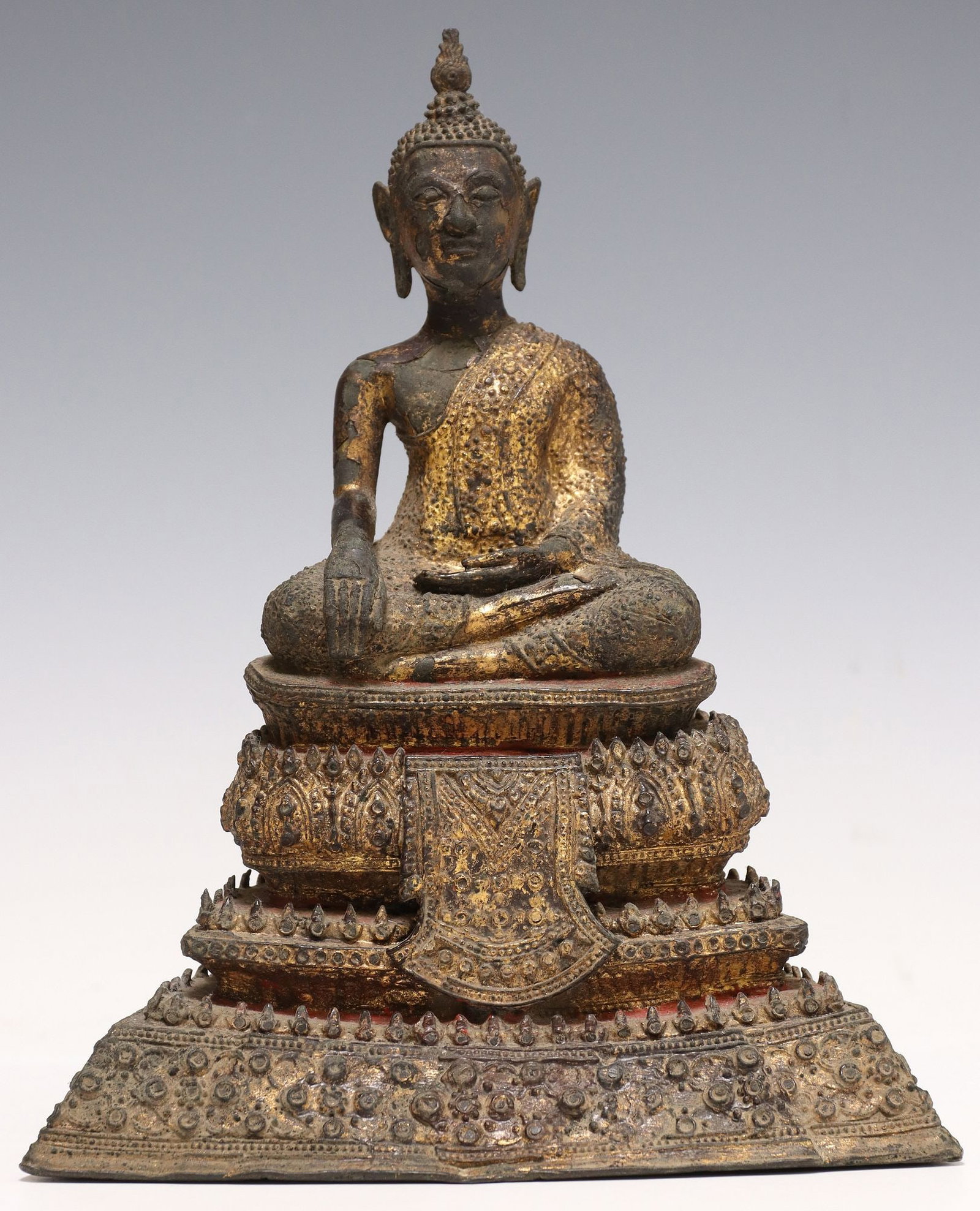 SOUTHEAST ASIAN PATINATED METAL BUDDHA FIGURE, THAILAND: Southeast Asian patinated metal figure, Seated Buddha, Thailand, depicting figure seated in Bhumisparsha (earth touching) Mudra, rising on a stepped base, with red and gilt painted accents, approx 10&